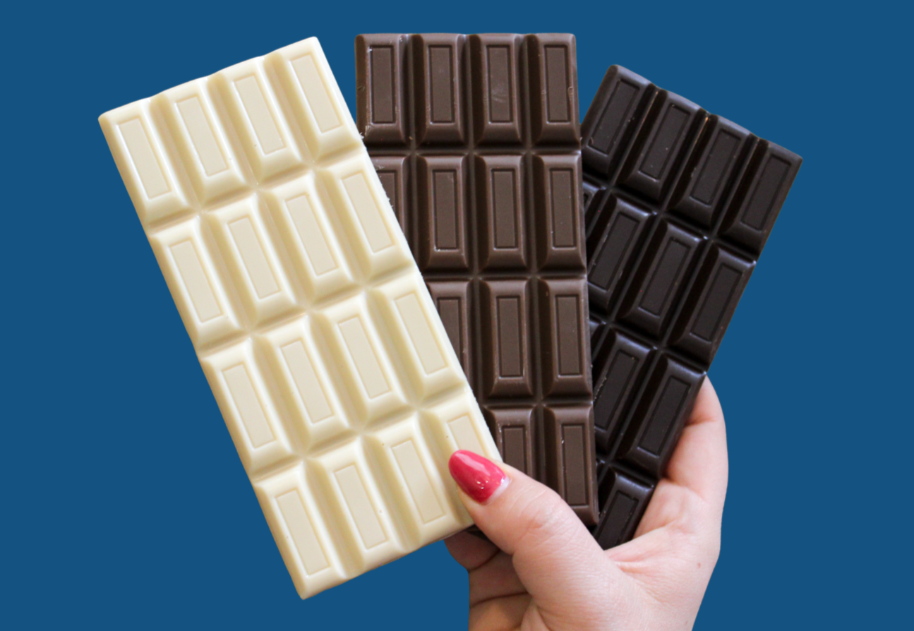 Hand holding three chocolate bars in white, milk, and dark chocolate varieties.
