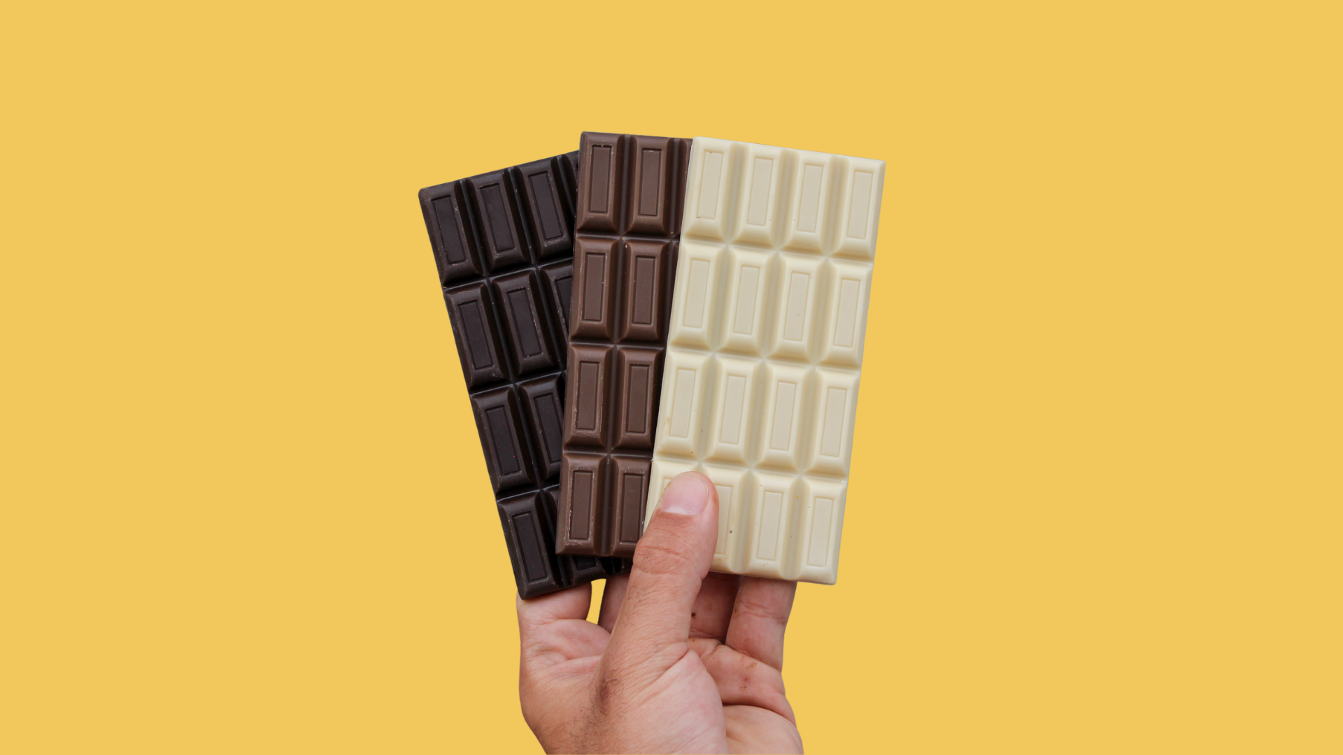Three Shine chocolate alternative bars in dark, light, and white varieties being held by a person's hand against a yellow background.
