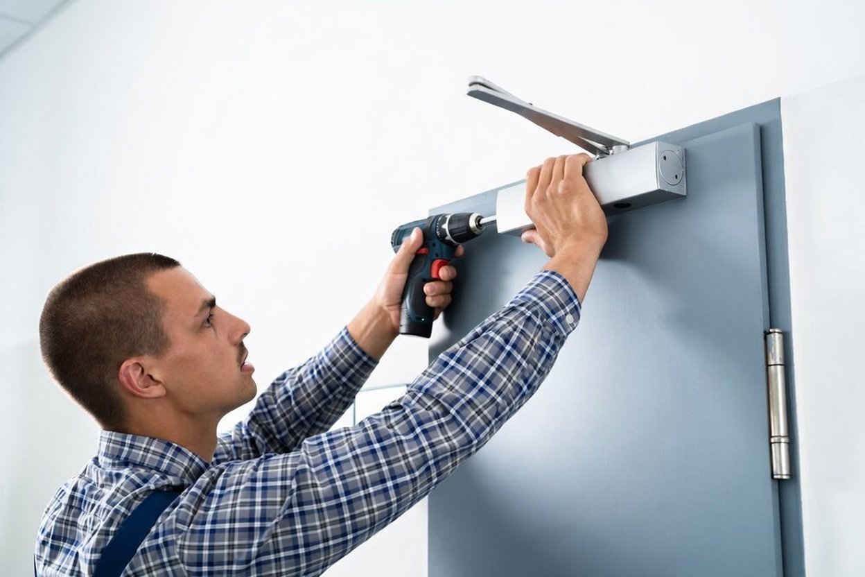 A man installing a sensor or device on a door frame using a drill