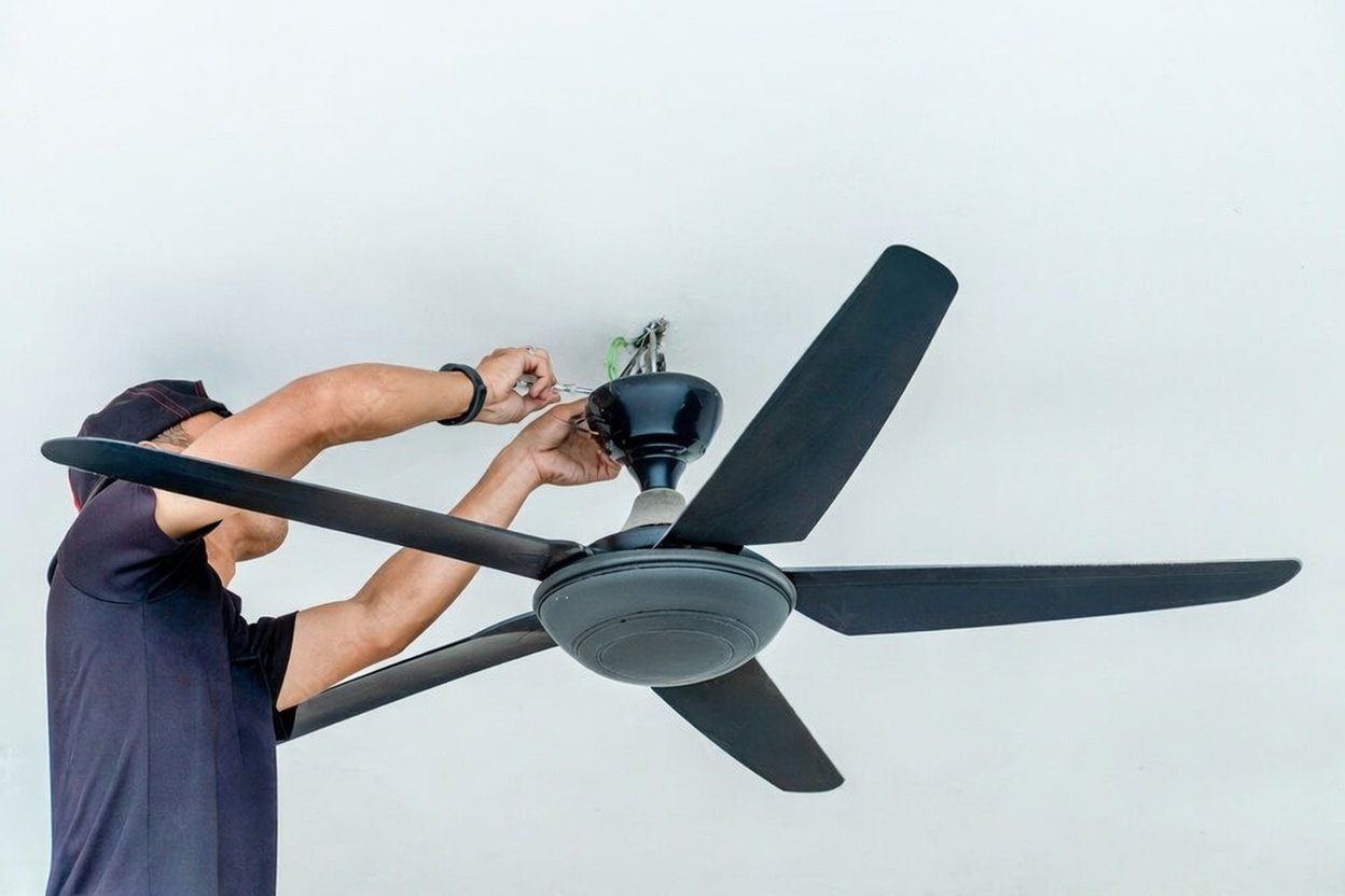 Person installing a ceiling fan on a white ceiling.
