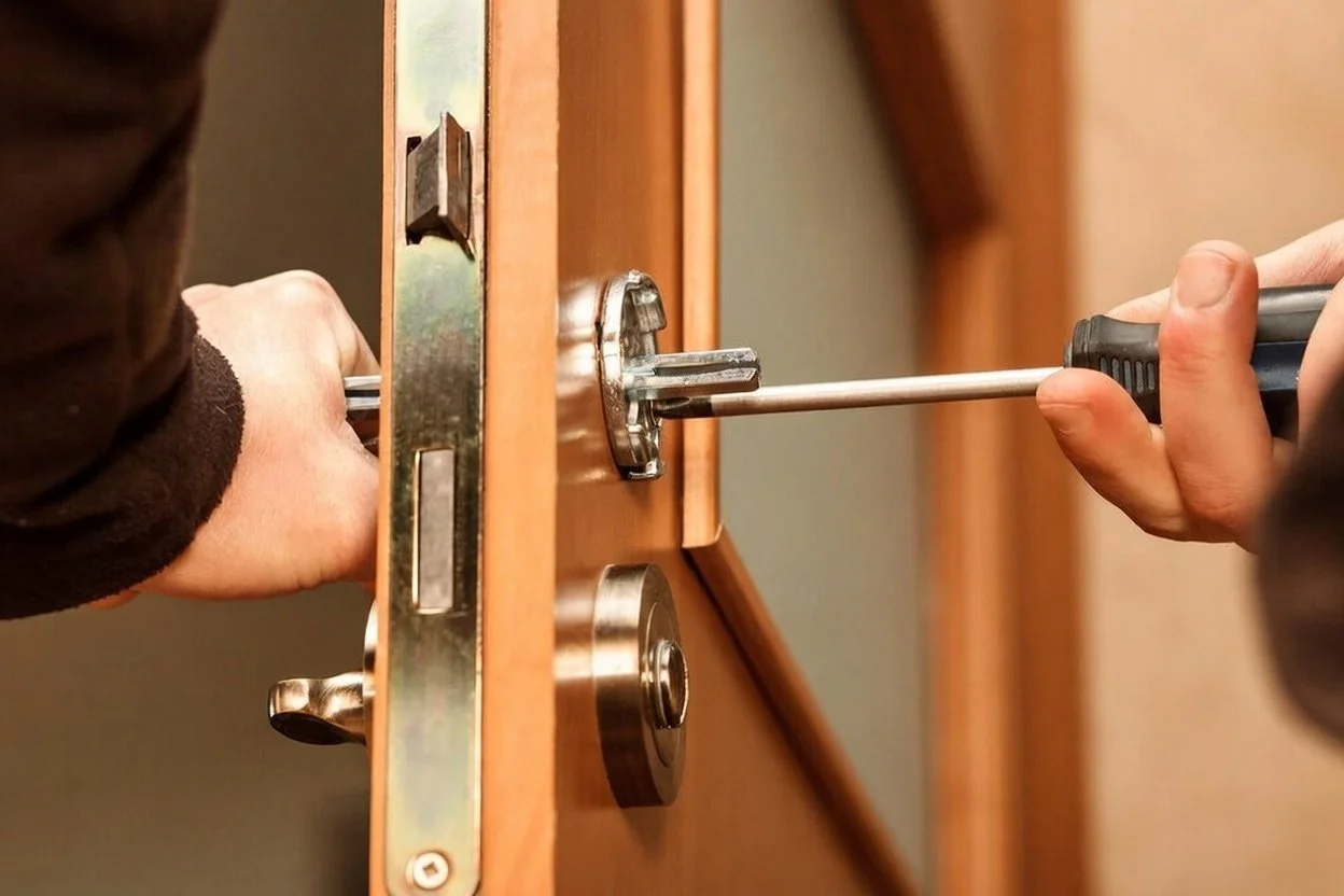 Person using a Phillips screwdriver to unlock a door with a circular lock and latch.