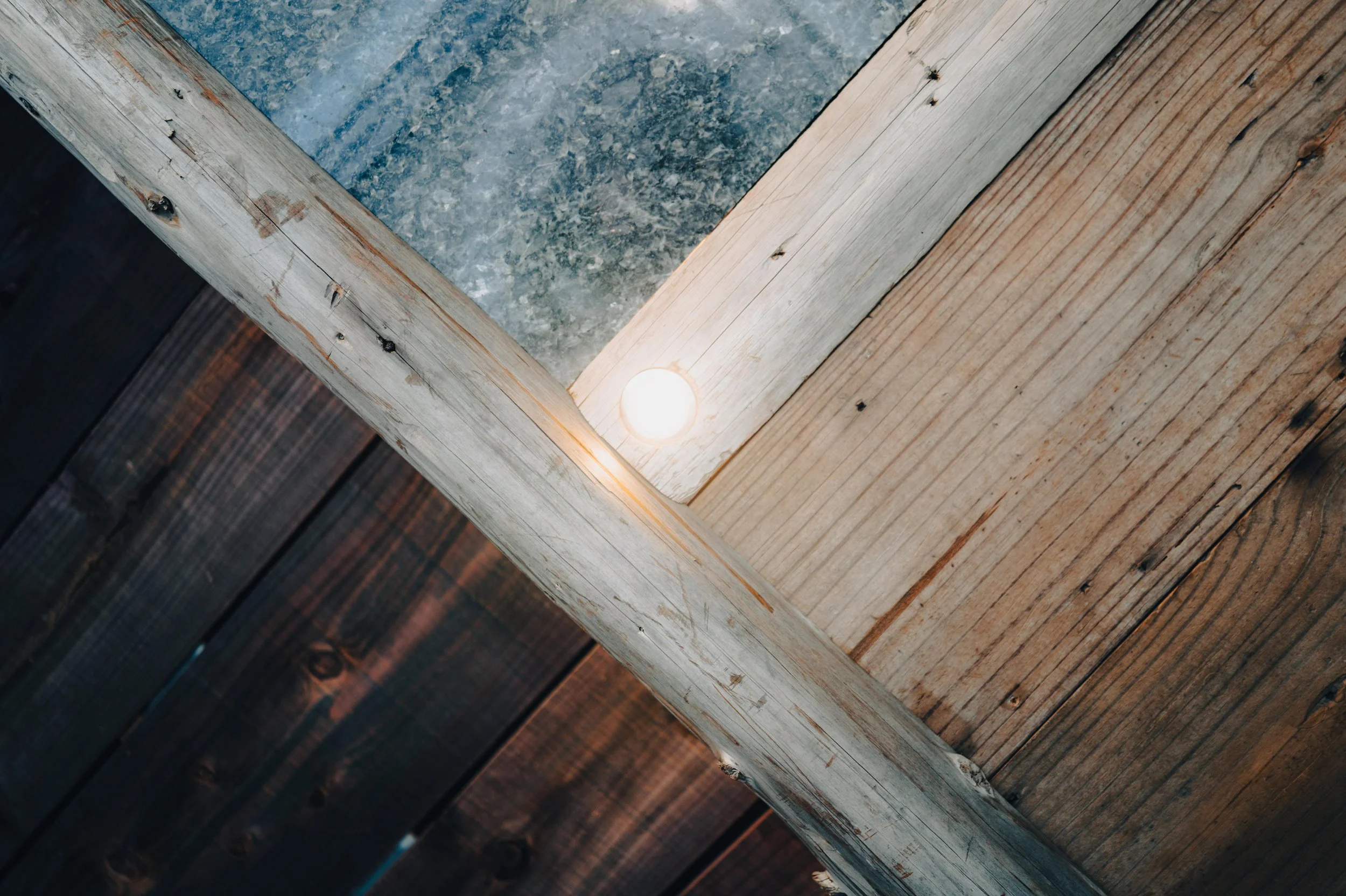Close-up of a wooden ceiling with a small round ceiling light and contrasting light and dark stained wooden beams.