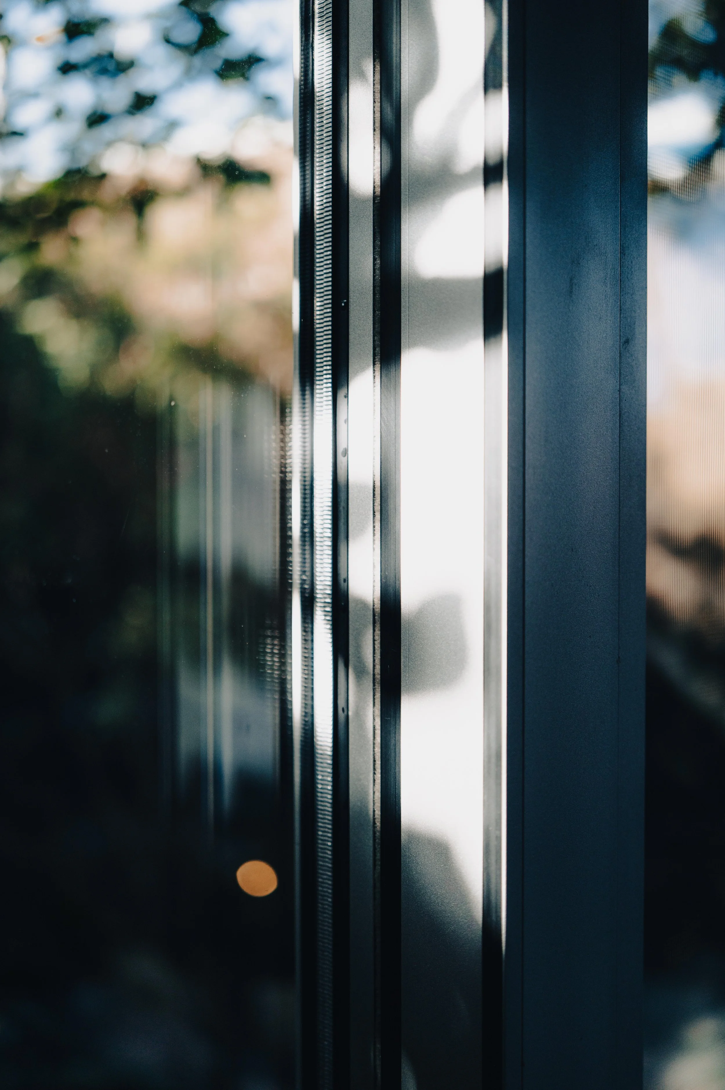 Close-up of a glass door with metal frame, sunlight casting shadows, and blurred outdoor background.