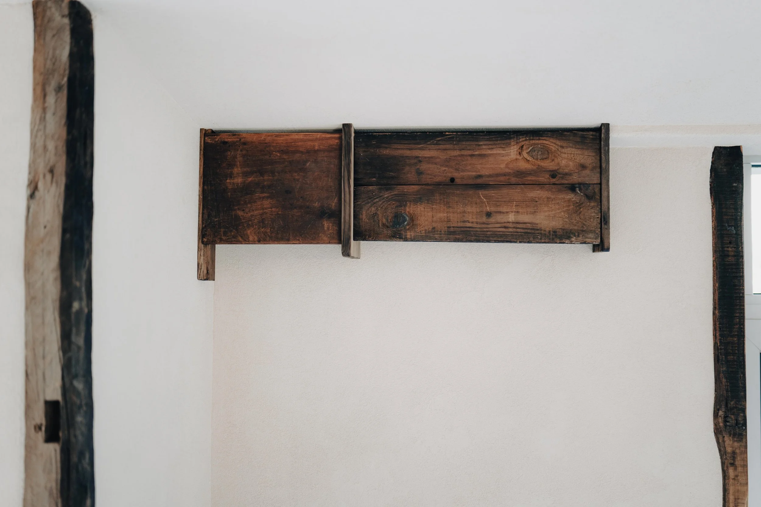 NUUT Aewol 눗애월 Close-up of a rustic wooden beam and wooden wall decoration on a white wall.