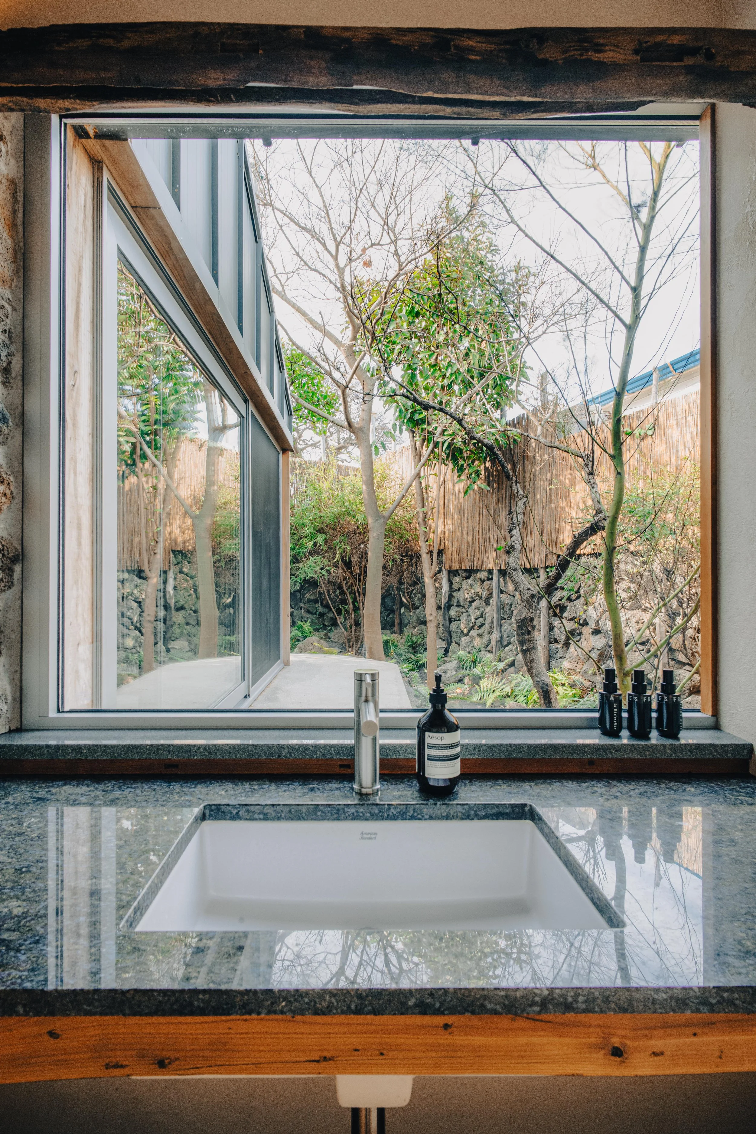 NUUT Aewol 눗애월A kitchen sink with a view of a garden through a large window, with bottles of soap on the counter.