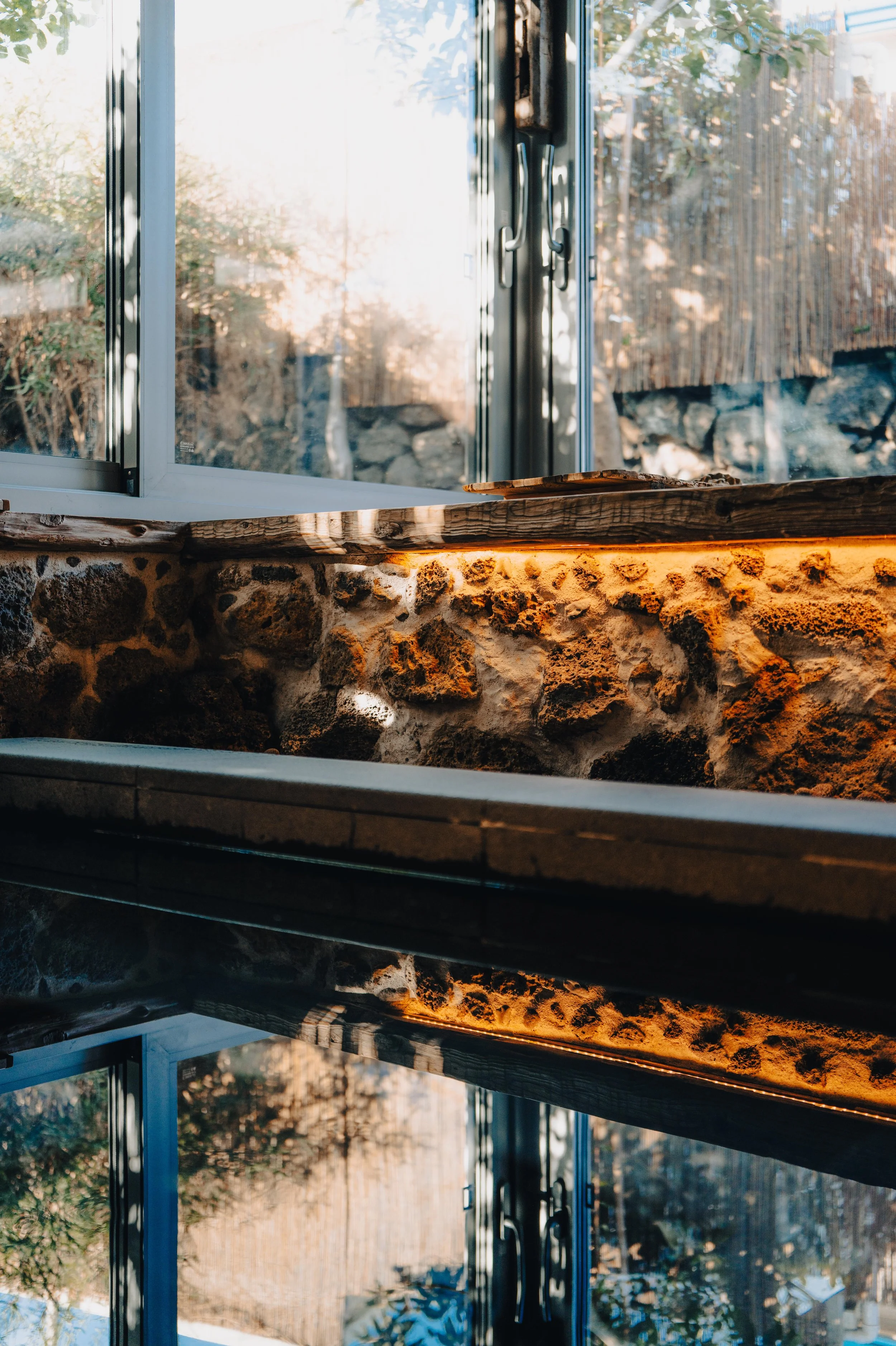 Open window with sunlight streaming in, revealing brick walls and a wooden surface inside a cozy room.