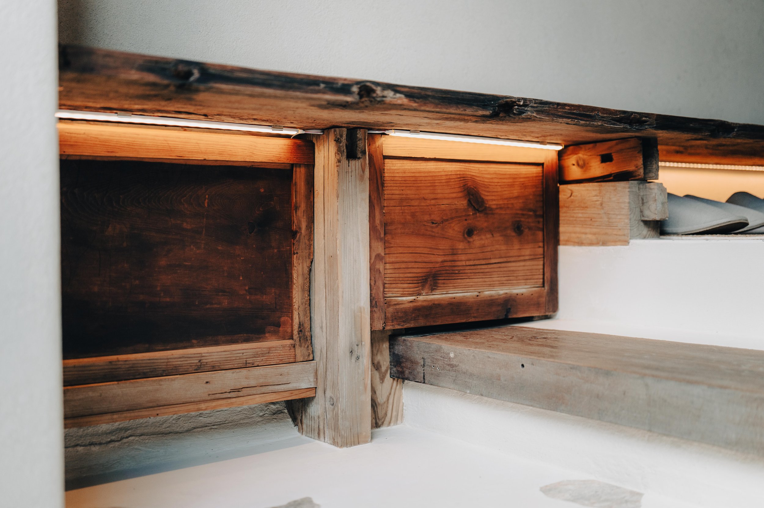 NUUT Aewol 눗애월 Close-up of wooden cabinets with LED lighting underneath, showing a mix of light and dark stained wood and some gray items on the right.