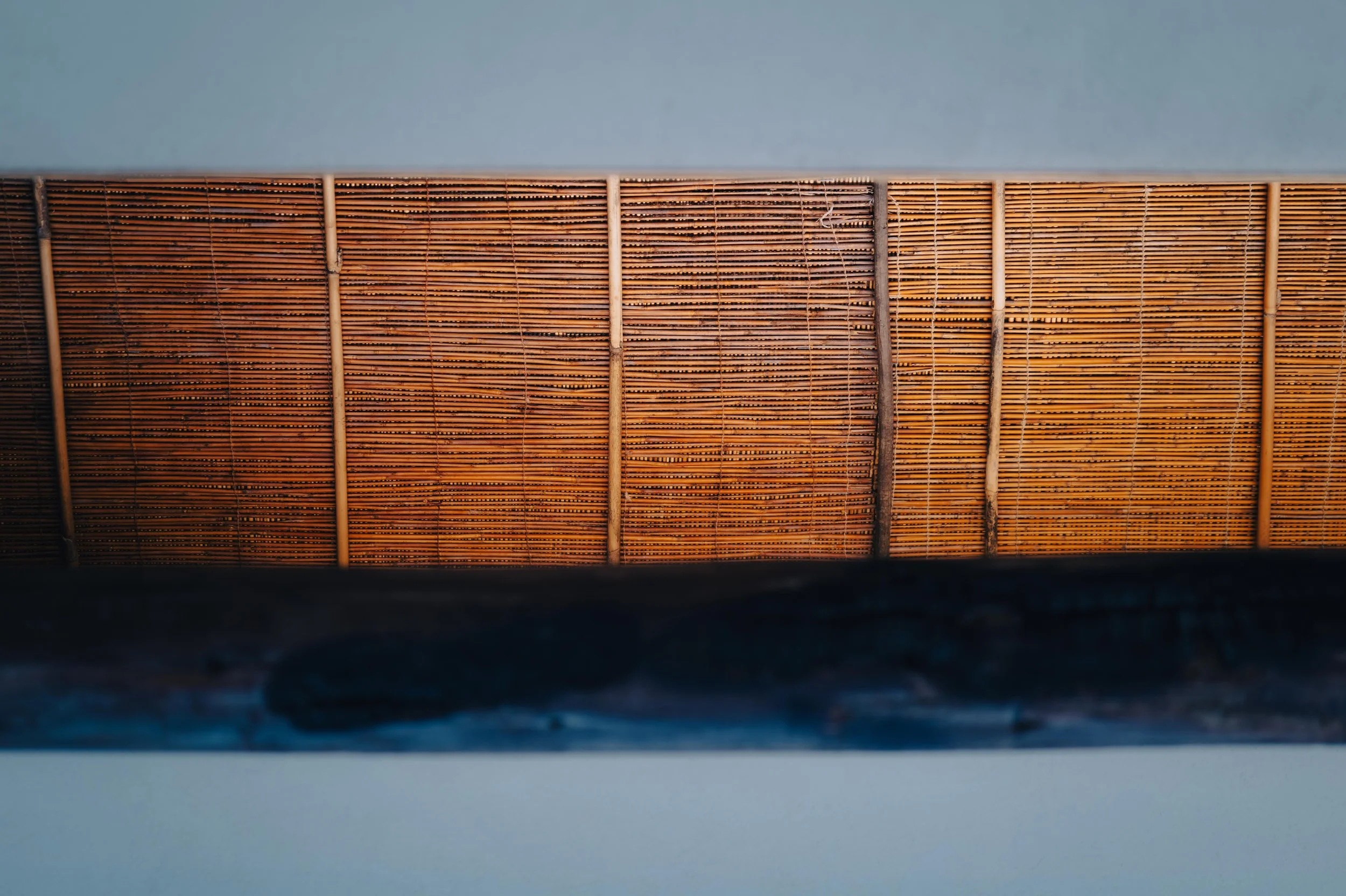 NUUT Aewol 눗애월 Close-up of a bamboo window blind with horizontal slats, partially obscured by a black object at the bottom of the frame.