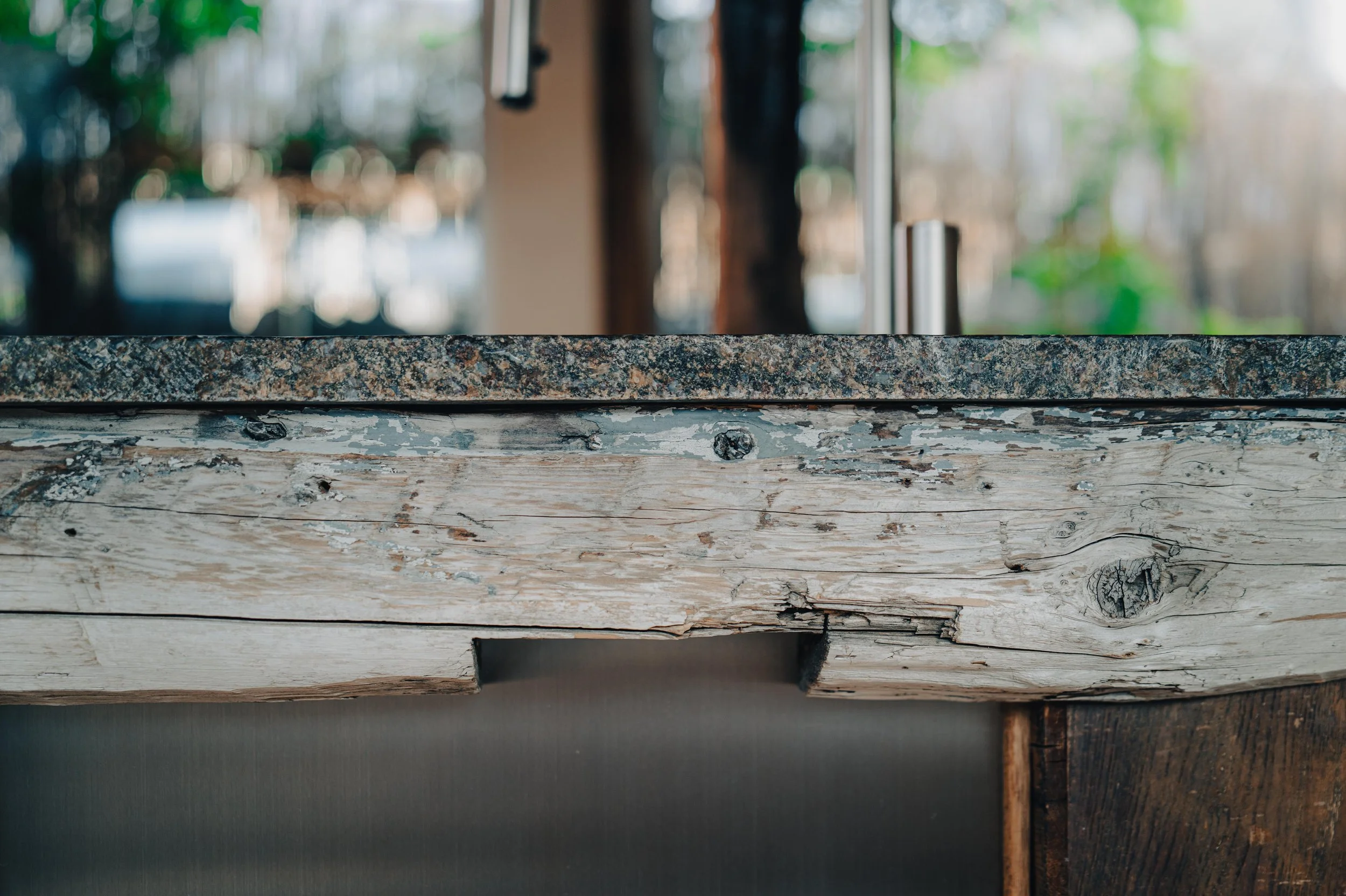 NUUT Aewol 눗애월 Close-up of a rustic wooden and stone countertop with a blurred background of window and trees outside.