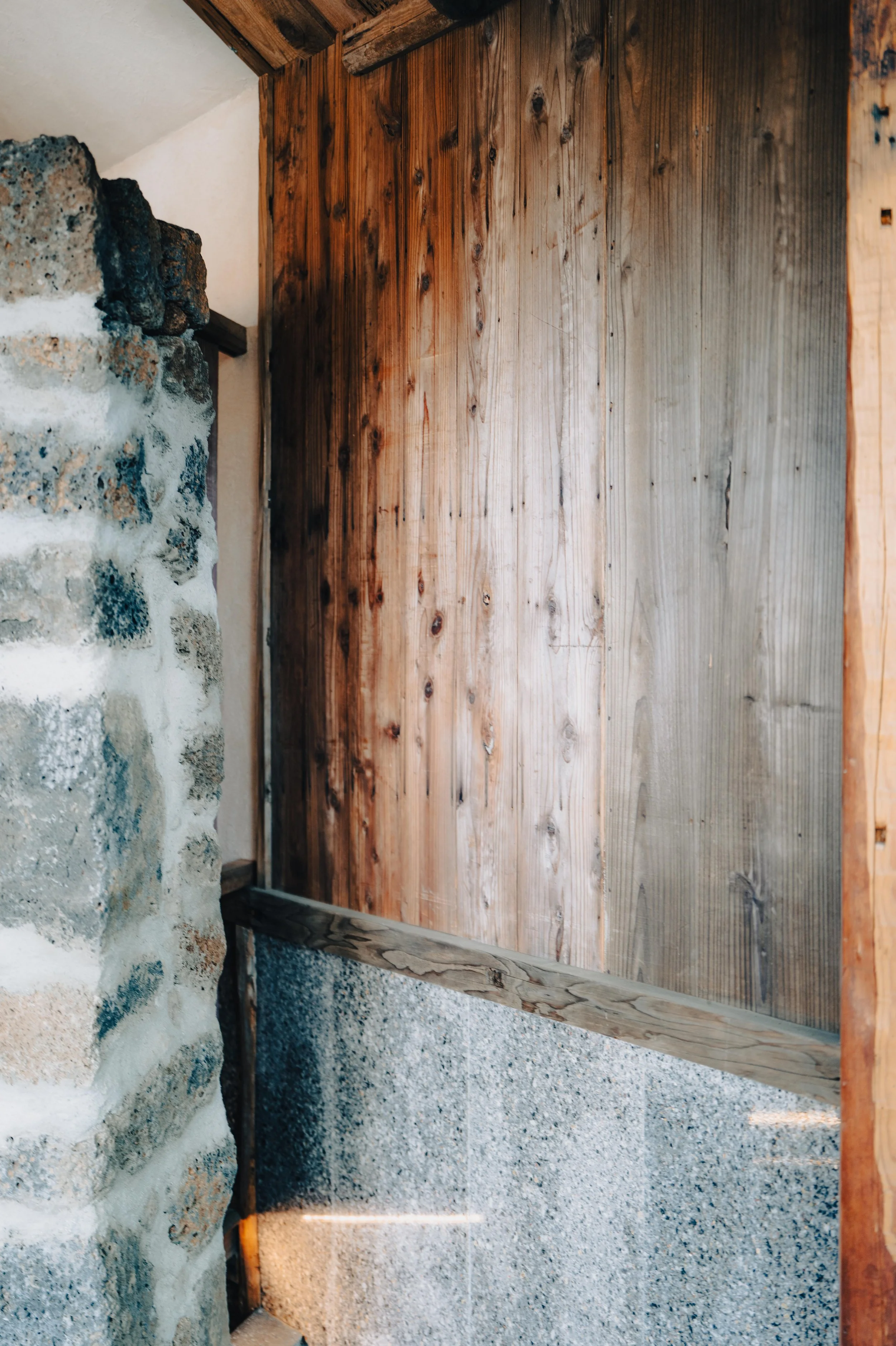 Interior corner of a room with a rustic stone wall, wooden paneling, and concrete flooring.
