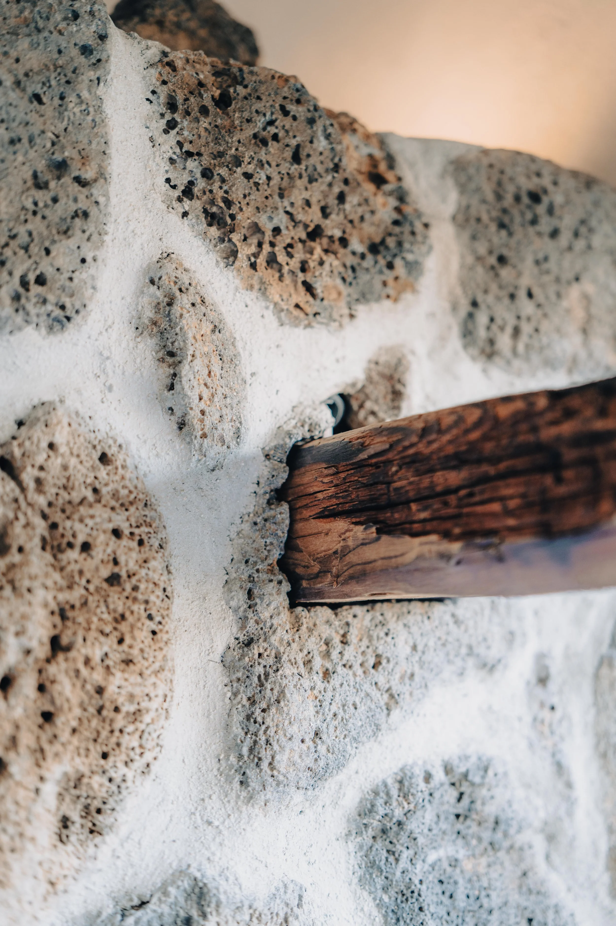 NUUT Aewol 눗애월Close-up of a textured wall made of white mortar and rocks, with a weathered wooden beam running through the middle.
