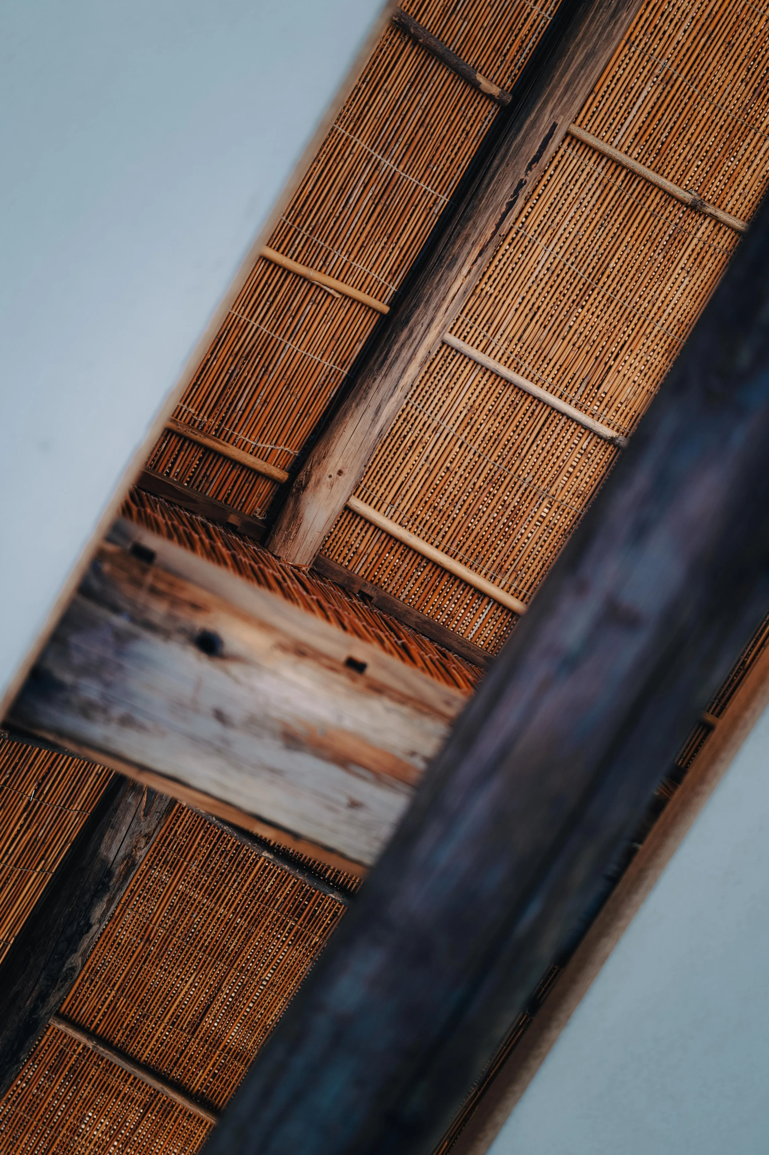 NUUT Aewol 눗애월 Interior view of a ceiling with bamboo roofing and wooden beams, seen from below.