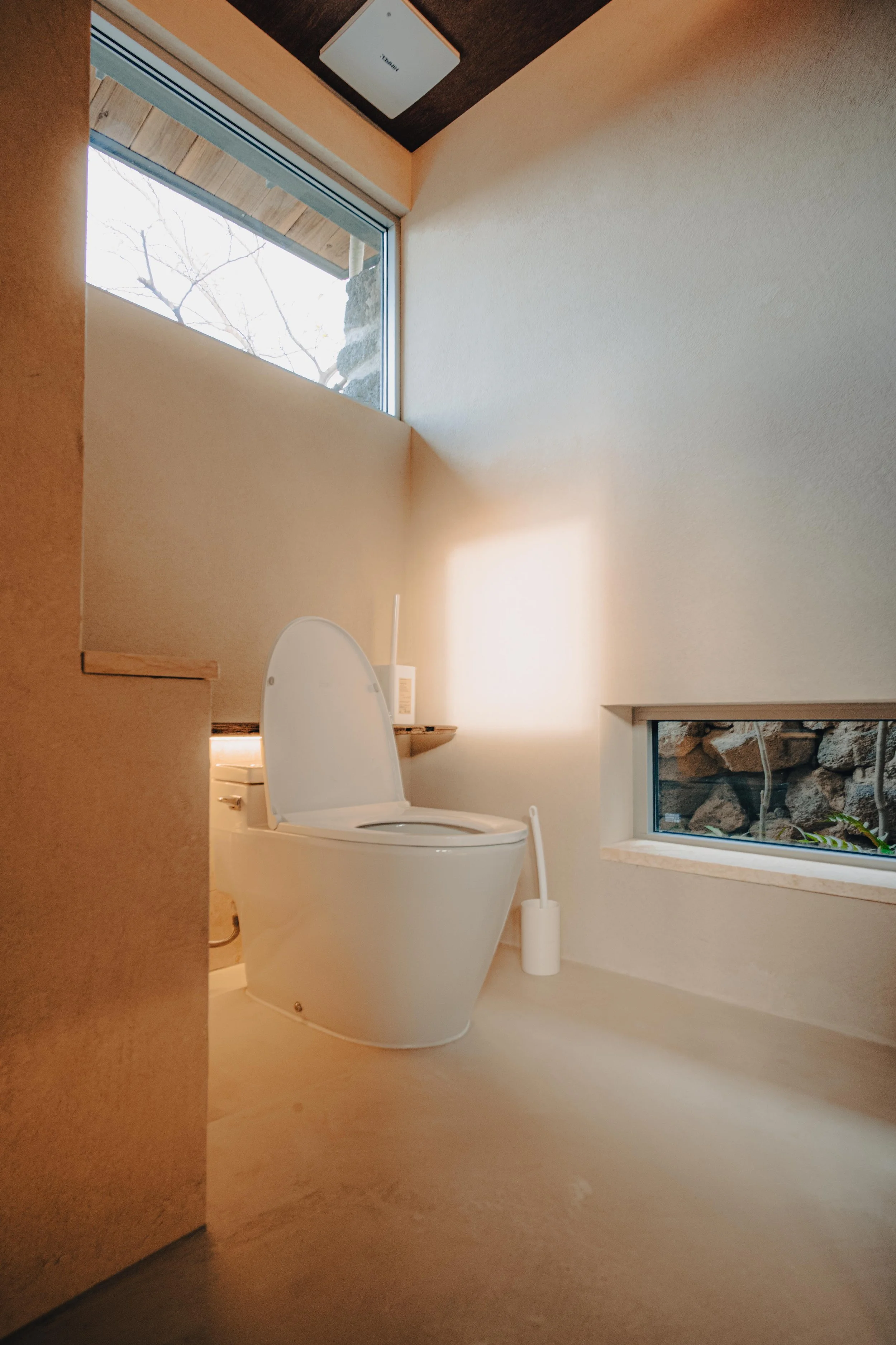 NUUT Aewol 눗애월 A modern, minimalist bathroom with a white toilet, a window low on the wall, and natural light illuminating the space.