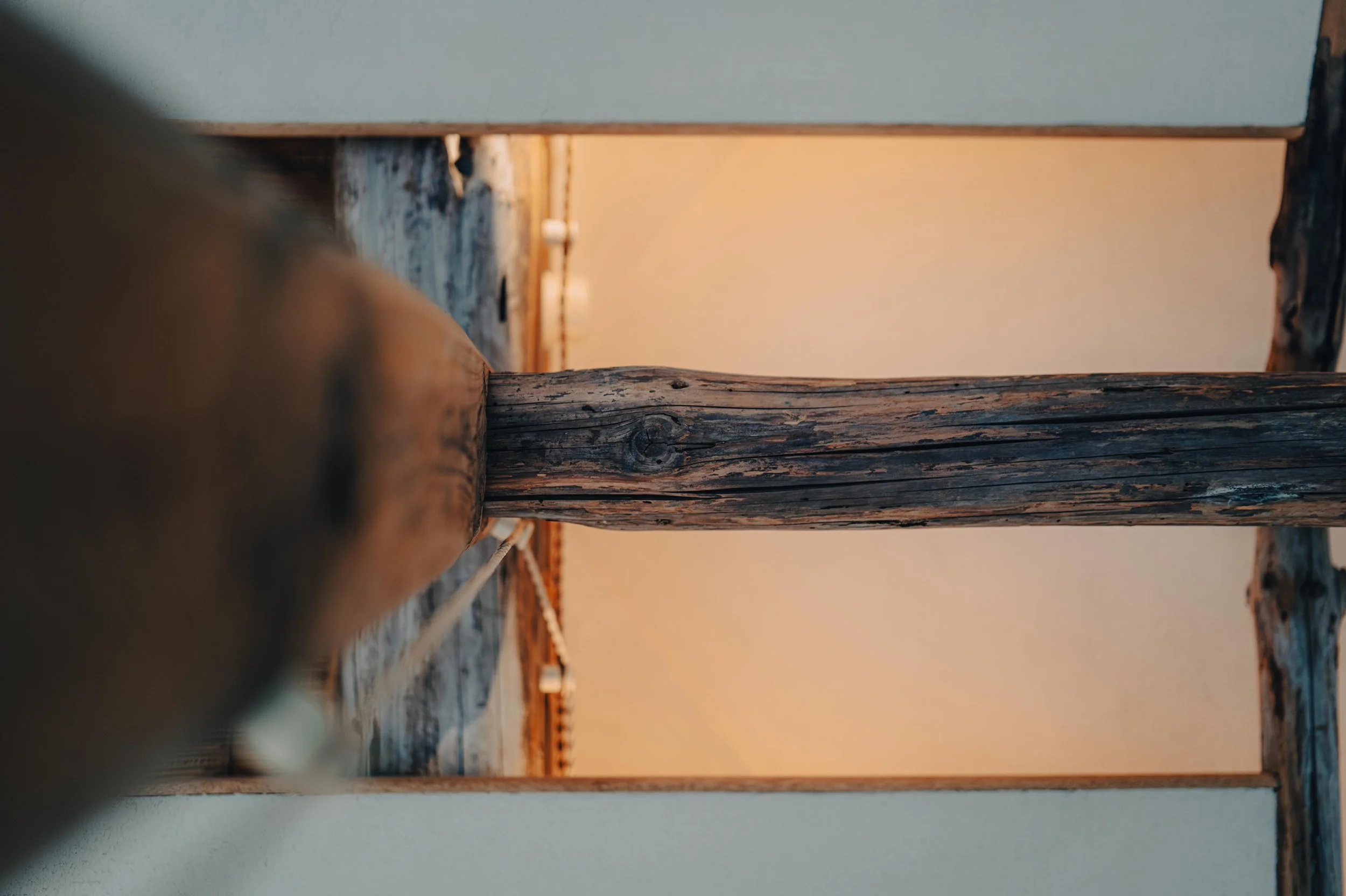 NUUT Aewol 눗애월 Close-up view of a wooden pole with a rustic appearance, with blurred background of wooden beams and white ceiling, in an indoor space.