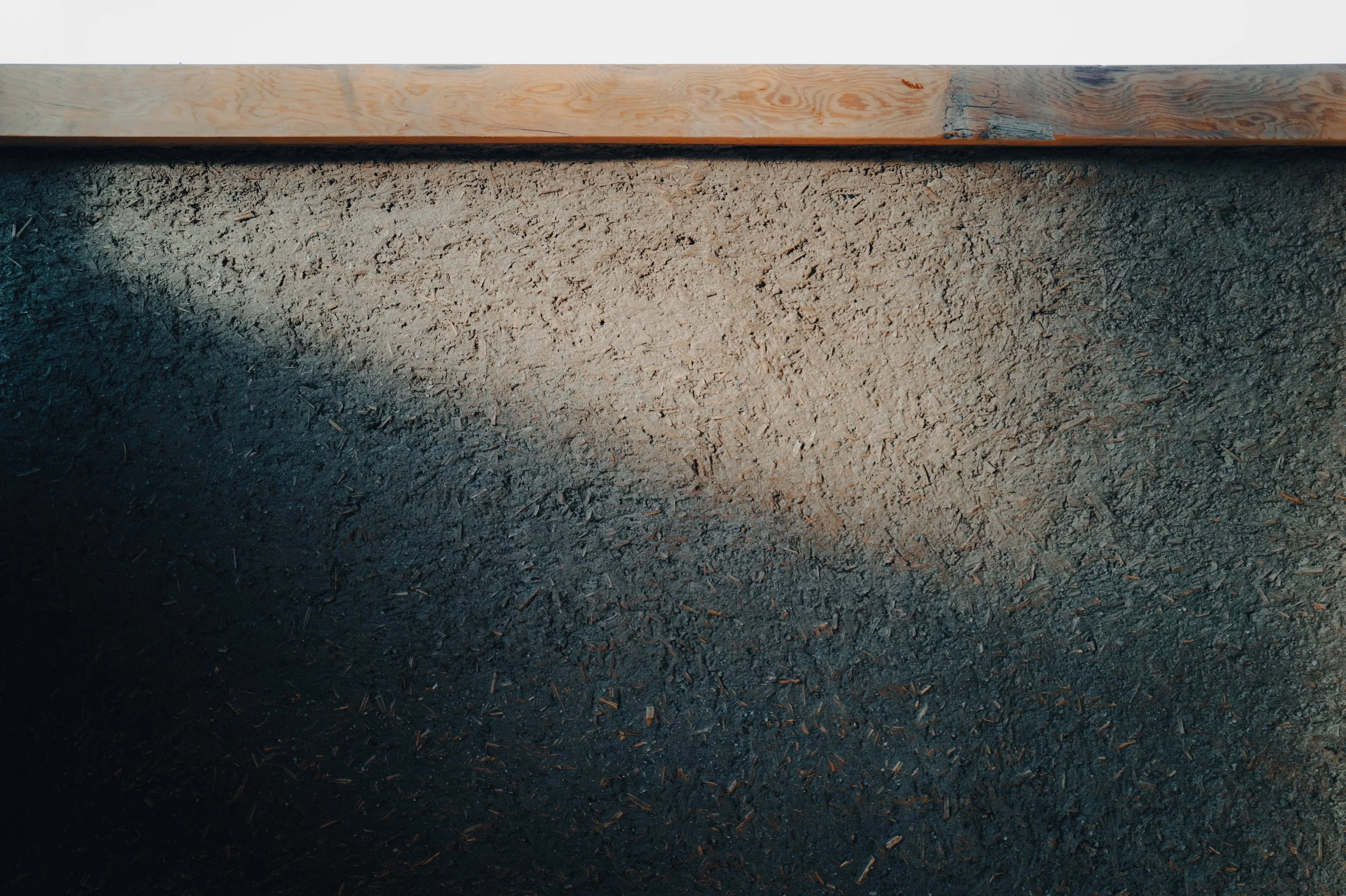 NUUT Aewol 눗애월 Close-up of a textured black asphalt surface with a wooden board at the top.