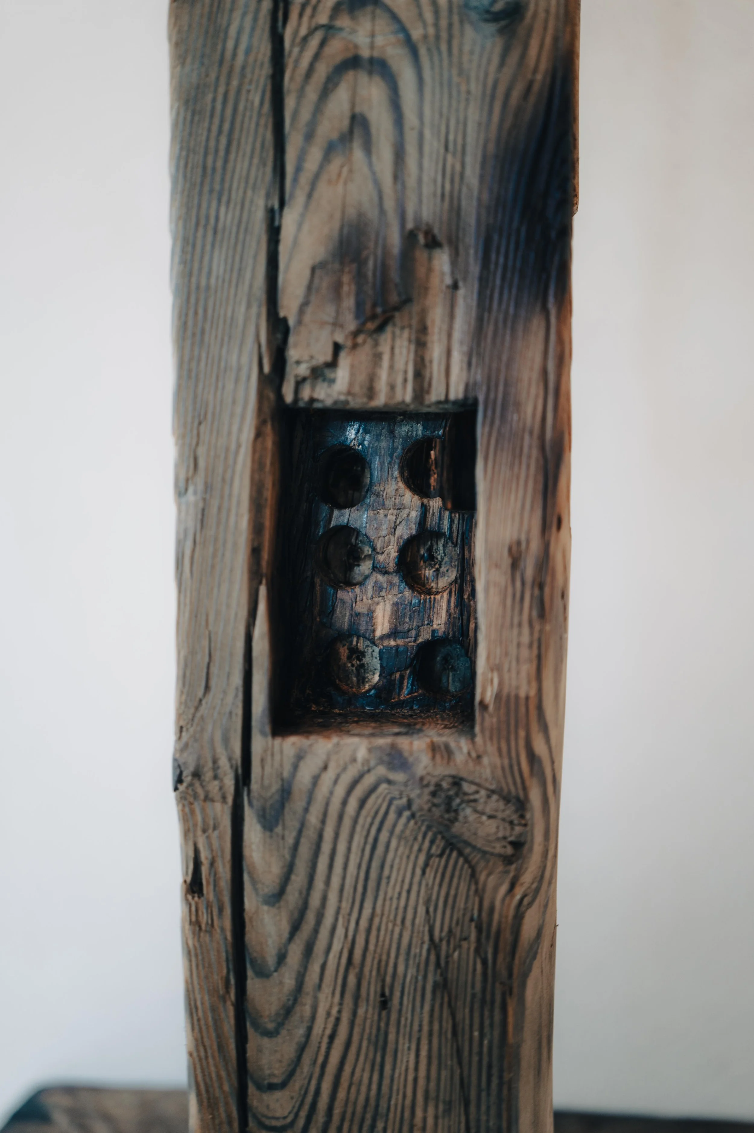 NUUT Aewol 눗애월 Close-up photograph of a weathered wooden beam with a square hole containing metal nails.
