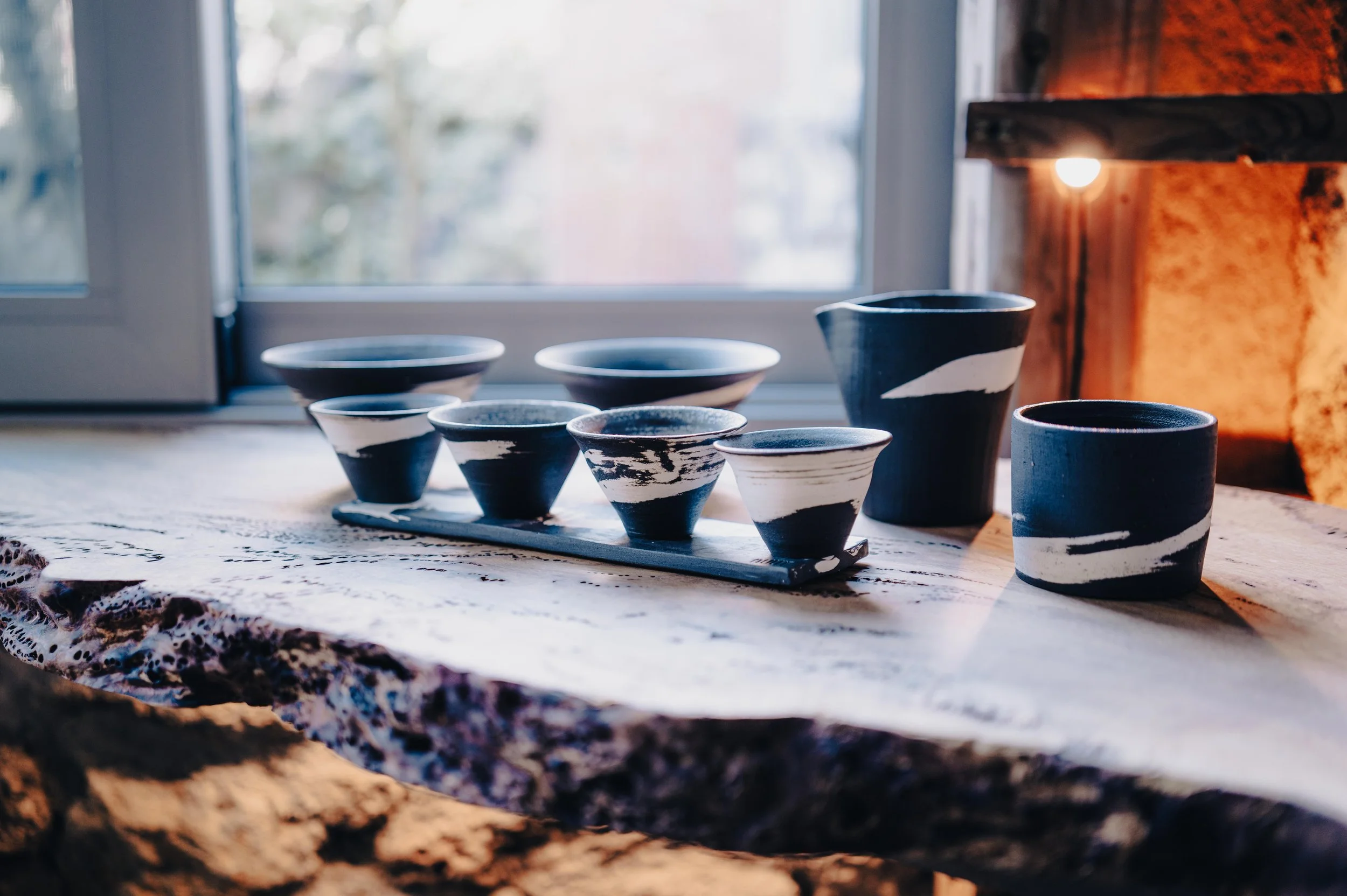 A collection of black and white ceramic cups and bowls on a wooden table near a window.