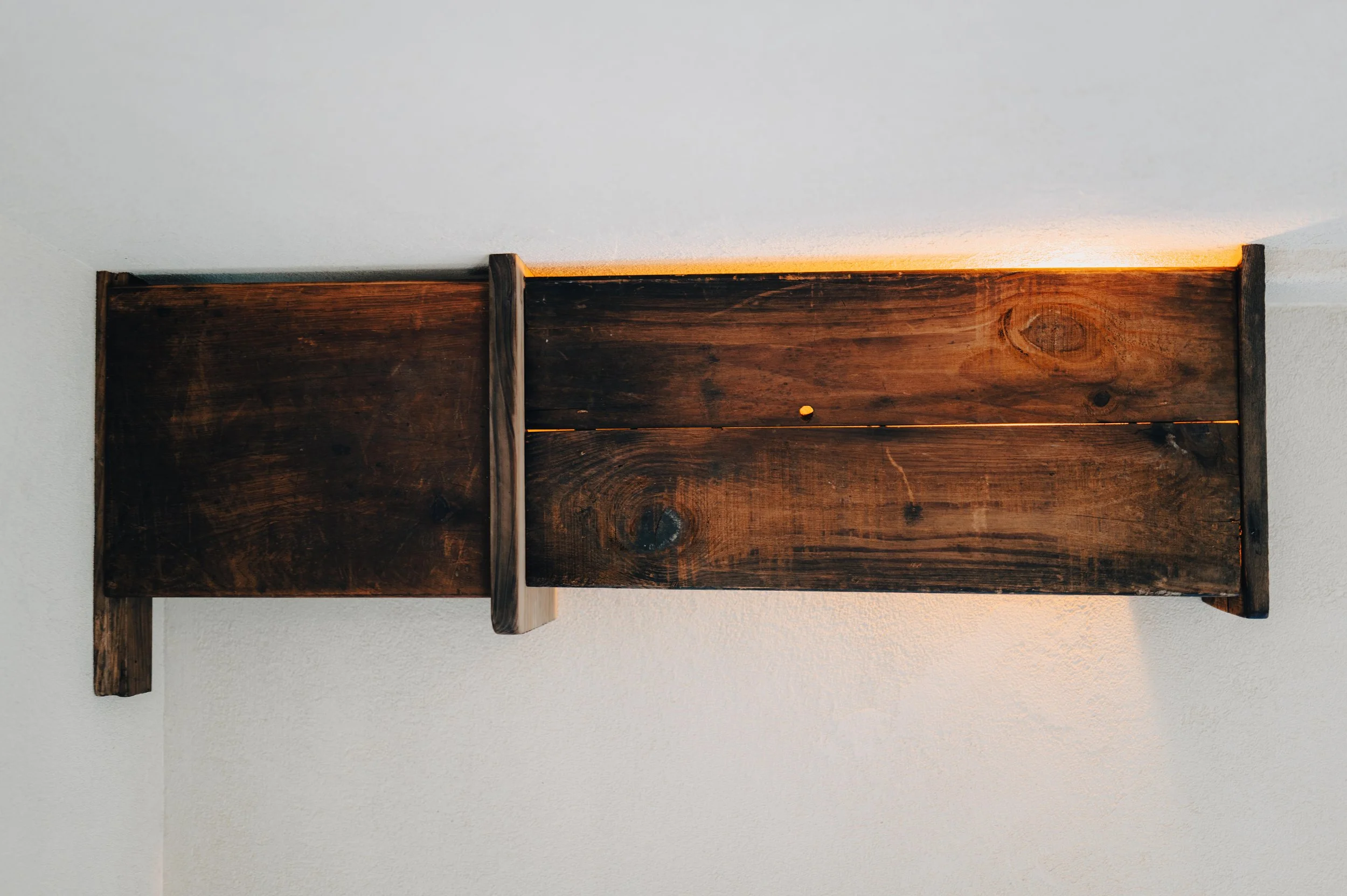 NUUT Aewol 눗애월 Wooden wall light fixture mounted on white wall with warm light shining from behind.