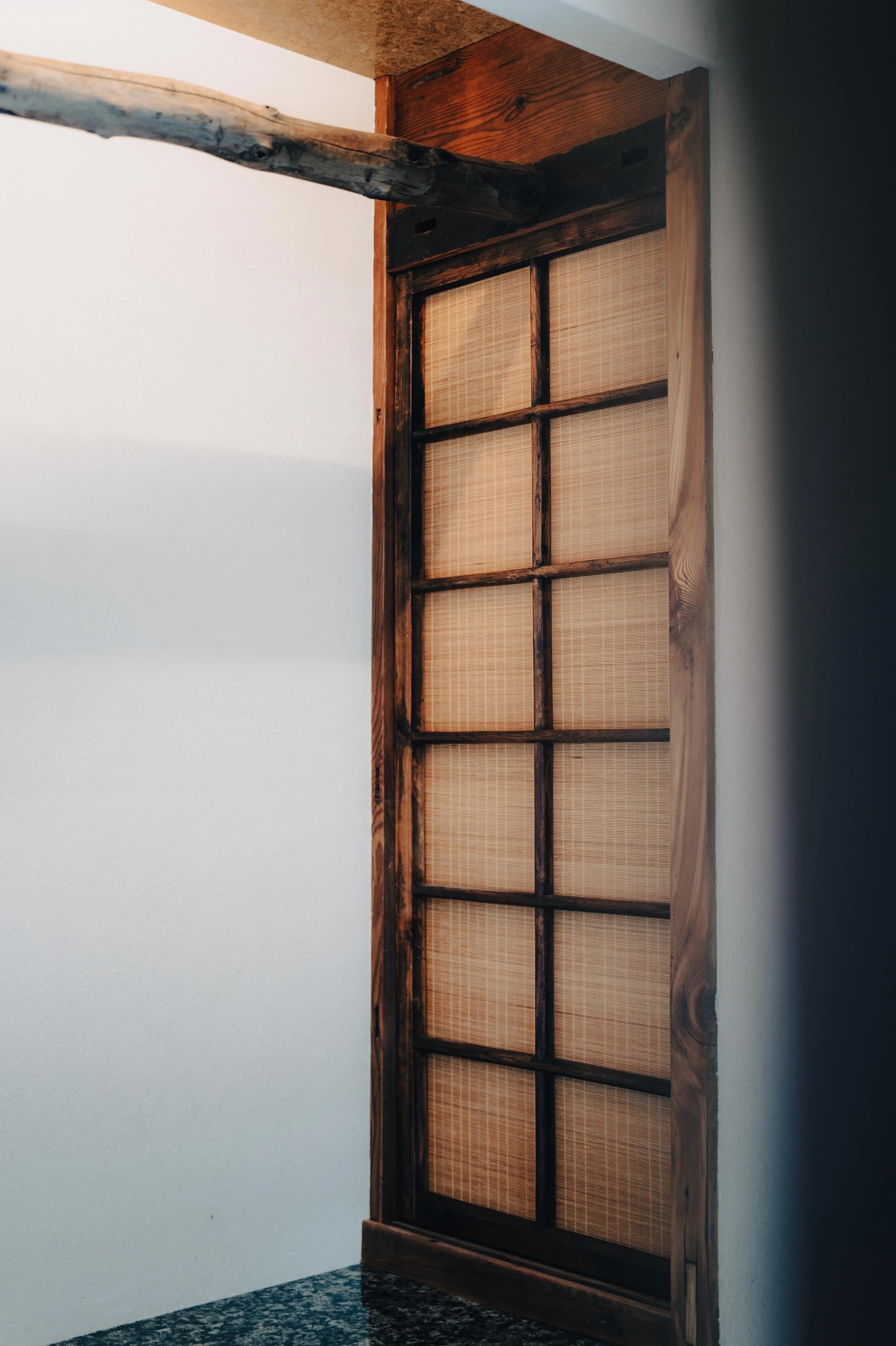 NUUT Aewol 눗애월 A wooden sliding door with a grid pattern, set in a room with white walls and a granite countertop.