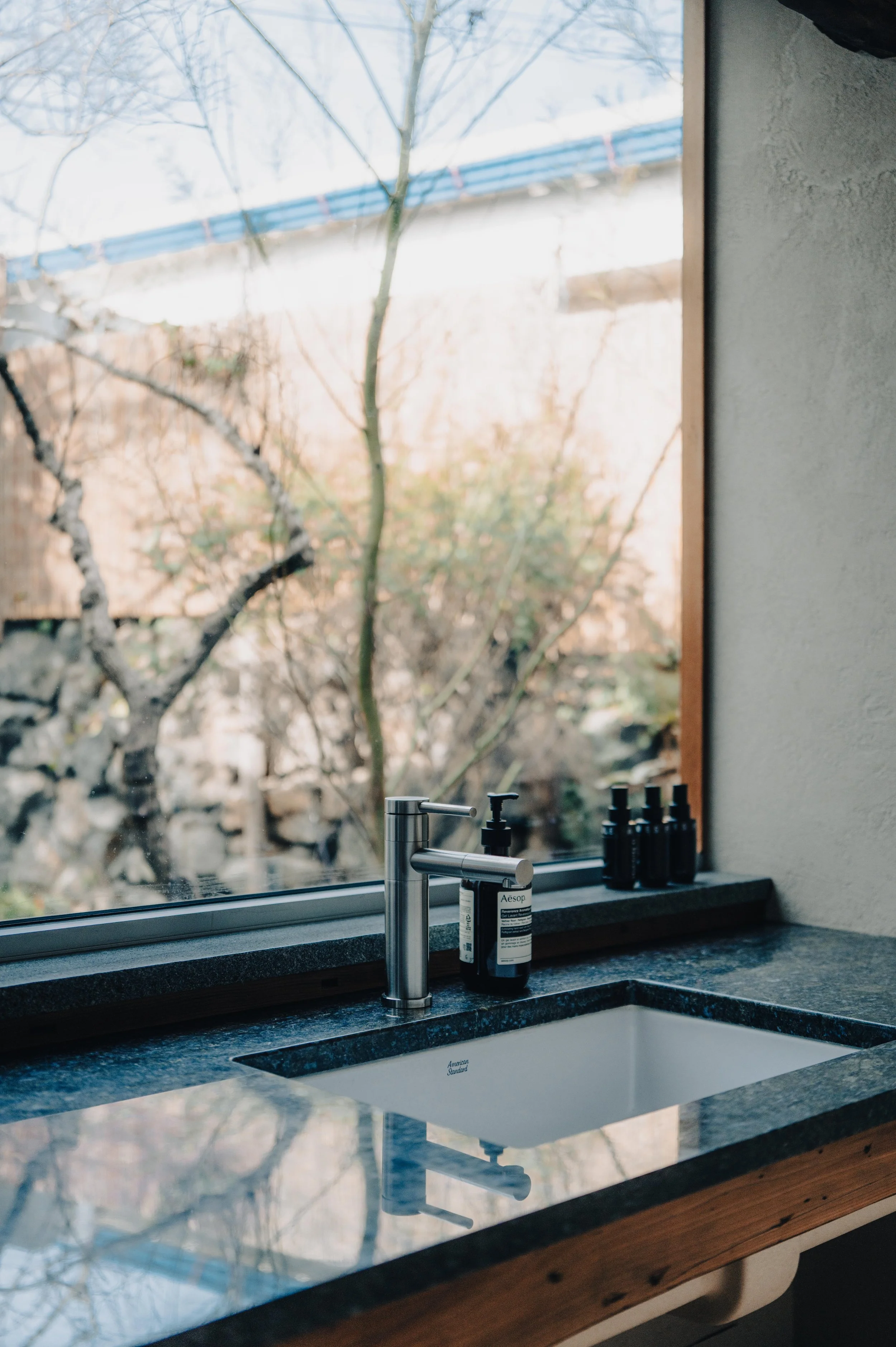 NUUT Aewol 눗애월 Kitchen sink with countertop, soap dispenser, and three bottles on the windowsill, with a view of trees outside the window.