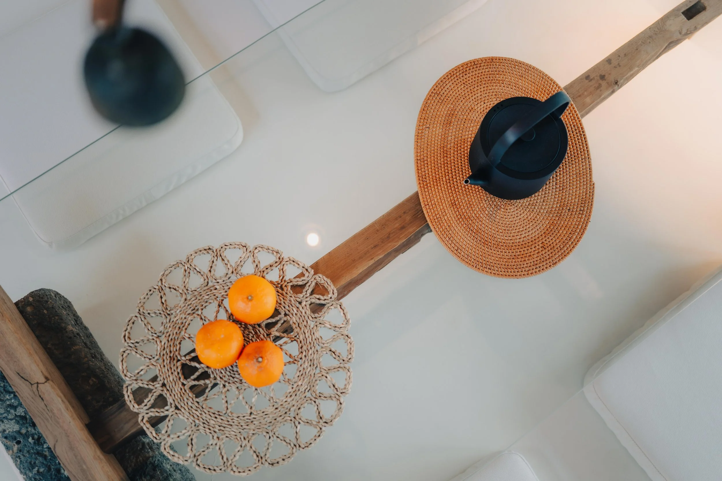 NUUT Aewol 눗애월 Top-down view of a white table with a woven basket containing three oranges, a black watering can on a round orange mat, and a mirror reflecting the table and objects.