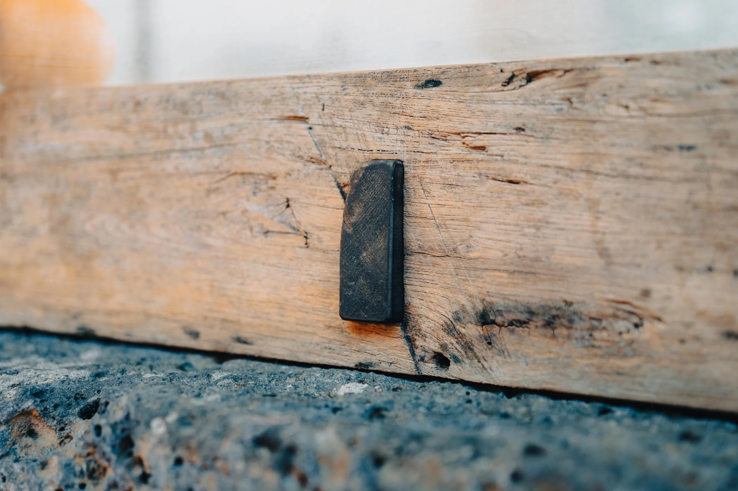 NUUT Aewol 눗애월Close-up of a black rubber wedge under a wooden beam resting on a stone surface.
