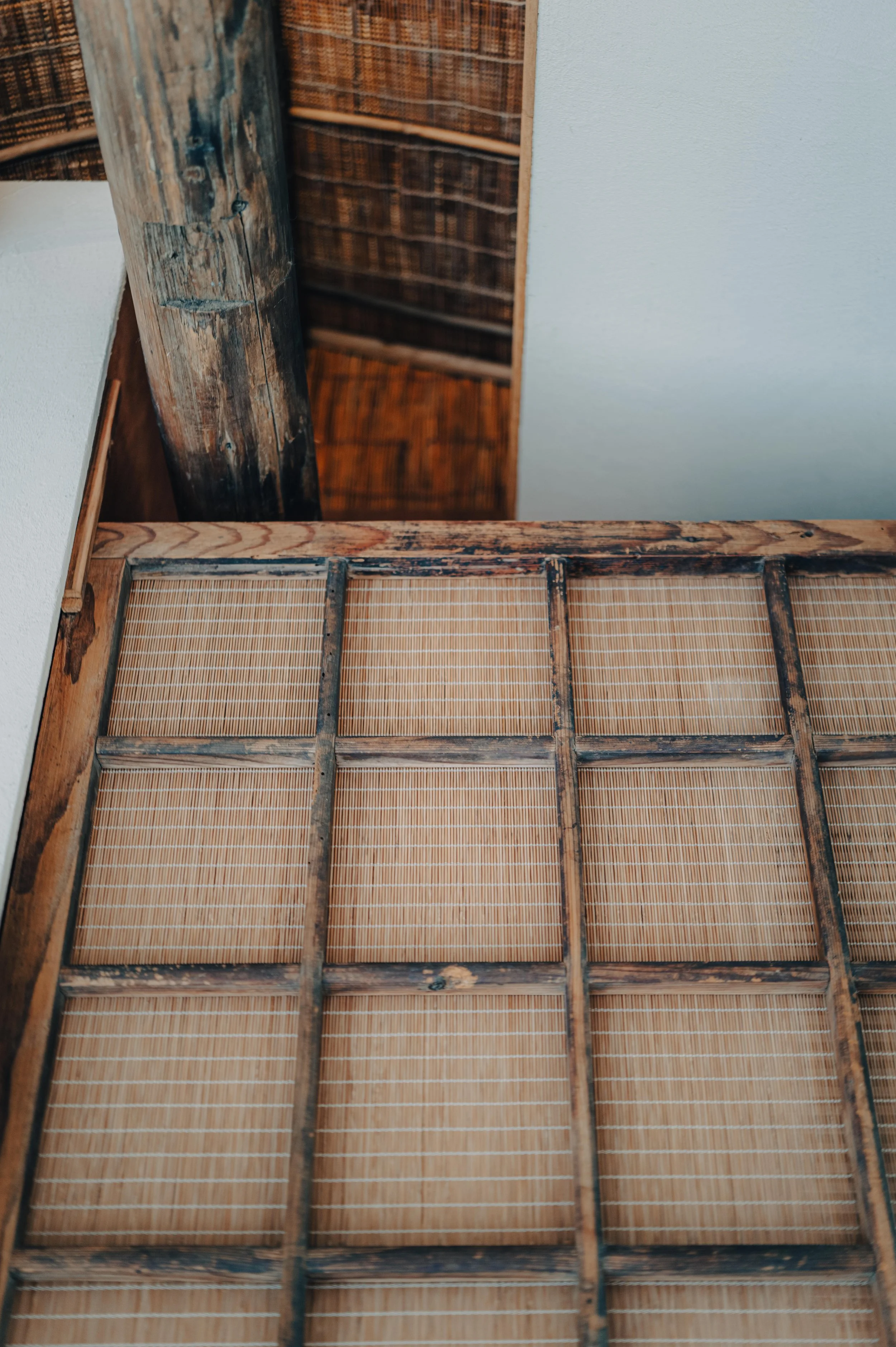 NUUT Aewol 눗애월 Part of a wooden and bamboo room divider or screen, with visible wooden frame and bamboo panels, against a white wall and wooden ceiling.