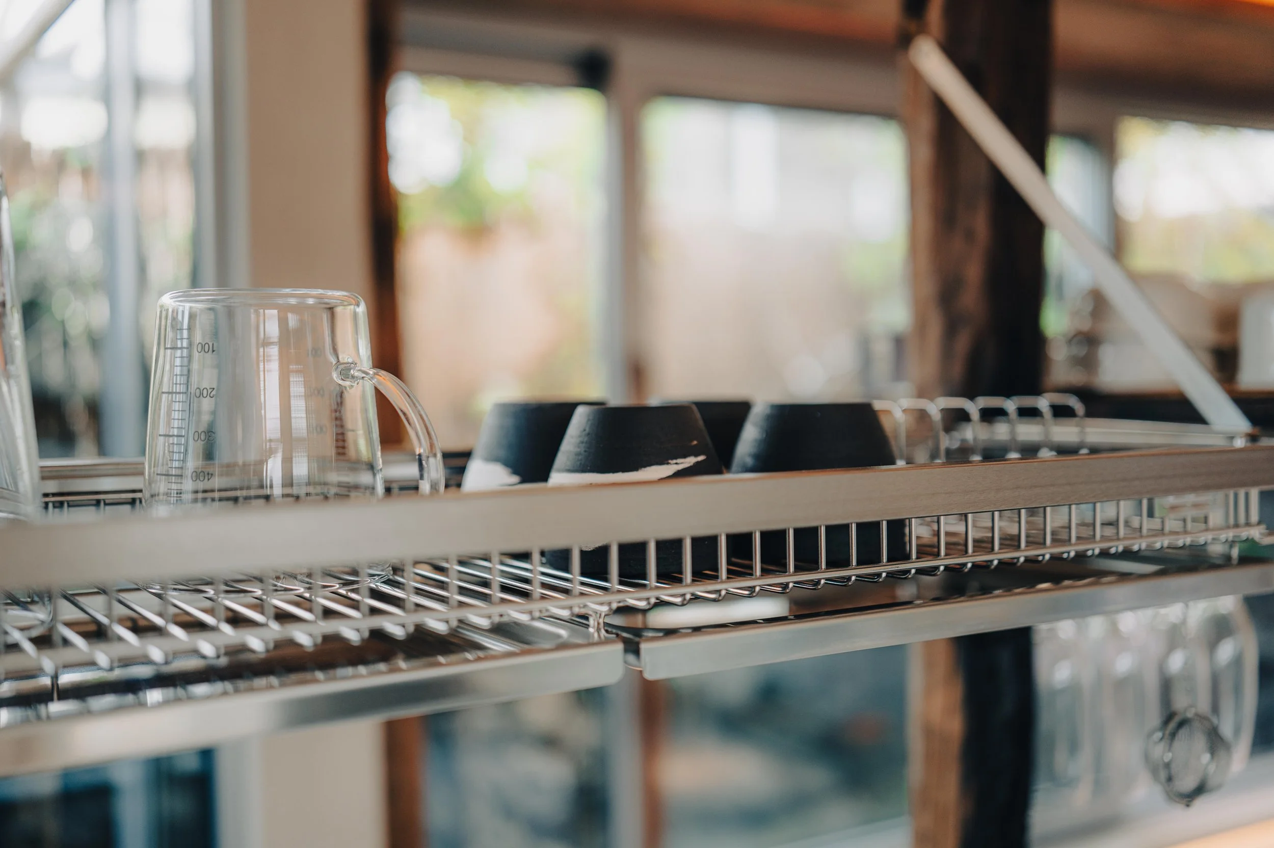 NUUT Aewol 눗애월 Dish drying rack with upside-down clear glass cups and black bowls inside a kitchen with large window