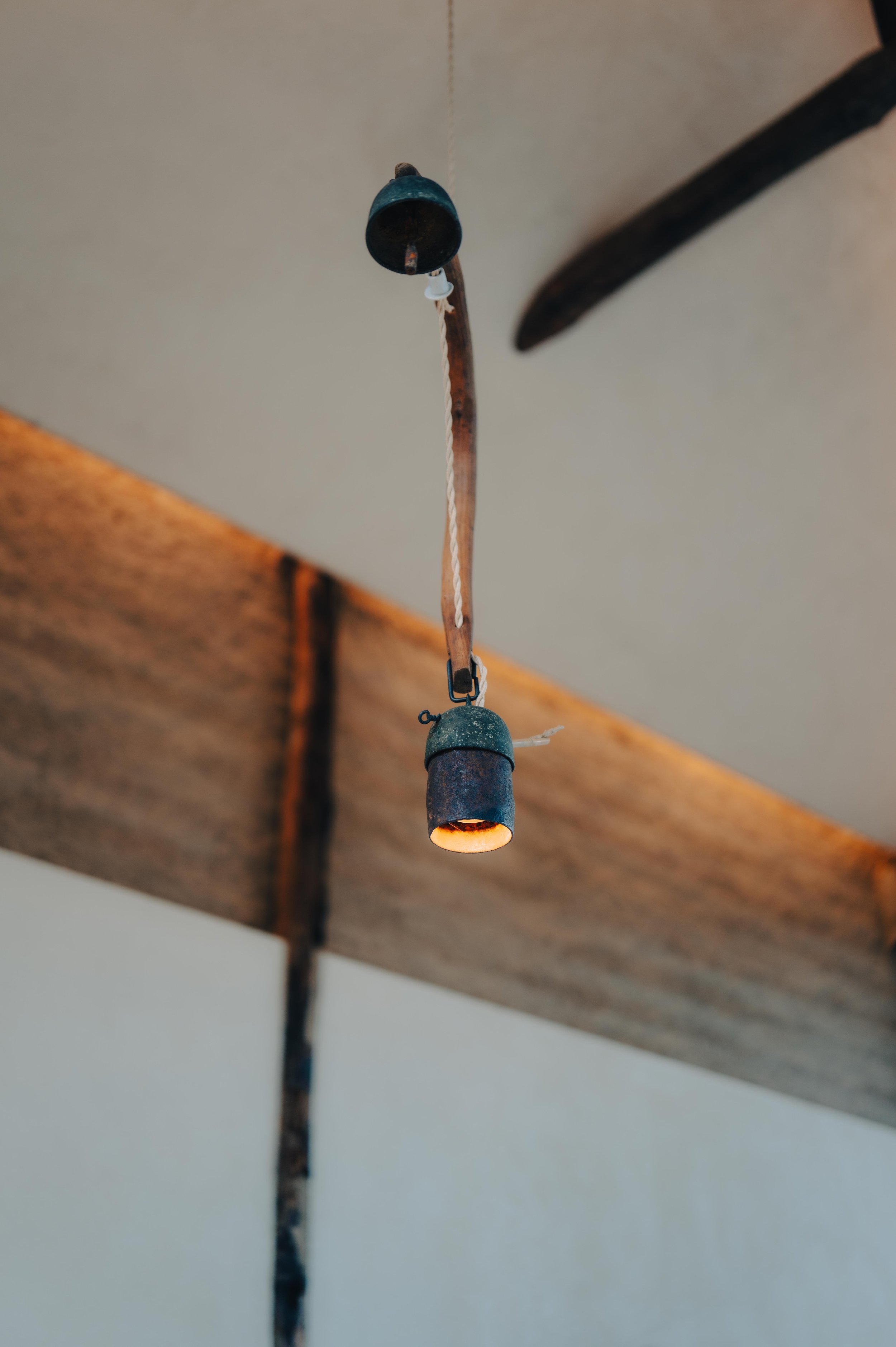 NUUT Aewol 눗애월 Vintage metal chandelier with a small candle-shaped light, hanging from the ceiling with a rope, against a wooden beam and ceiling background.