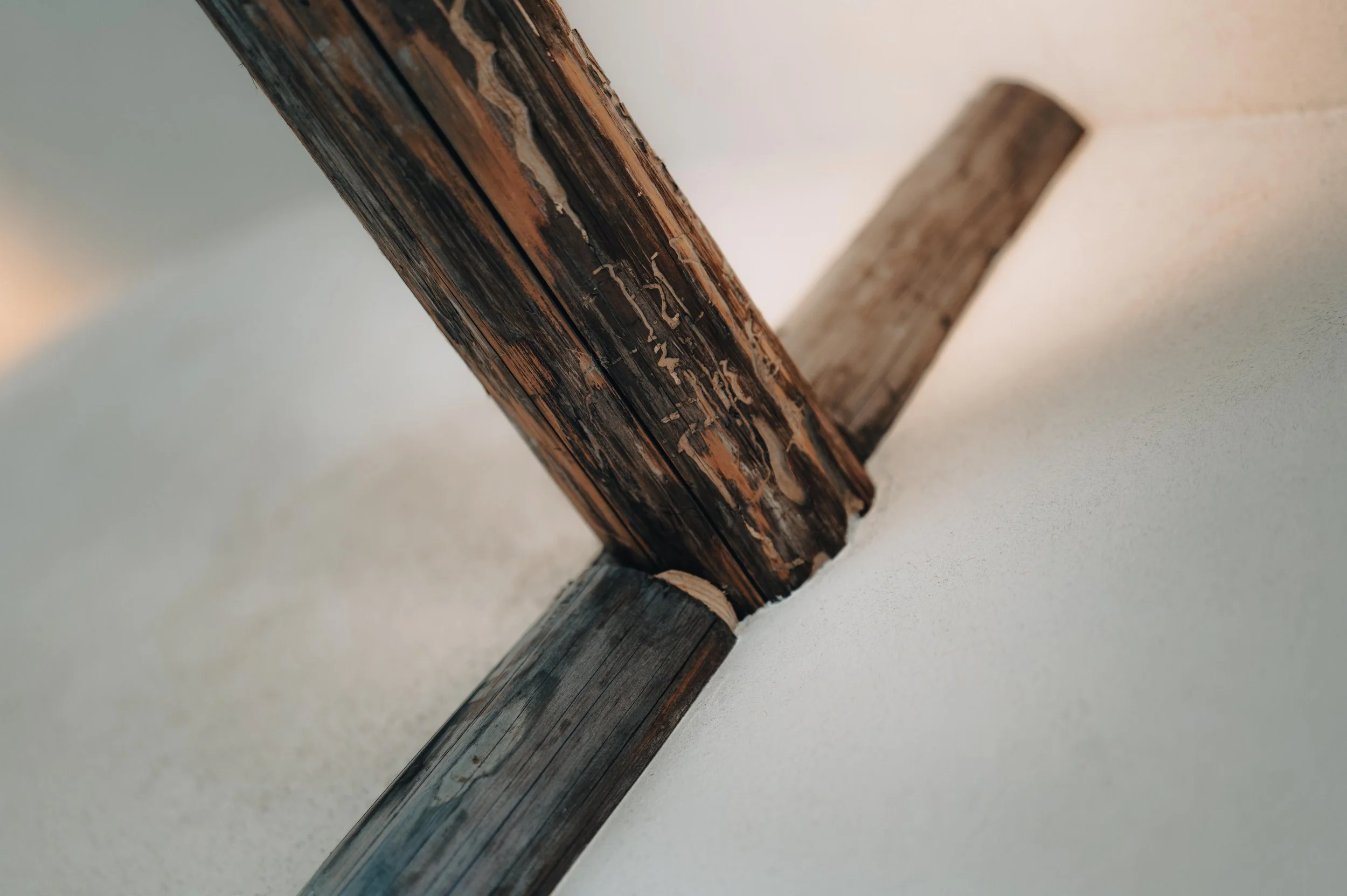 NUUT Aewol 눗애월 Close-up of a wooden beam attached to a white wall, showing weathered and peeling paint.