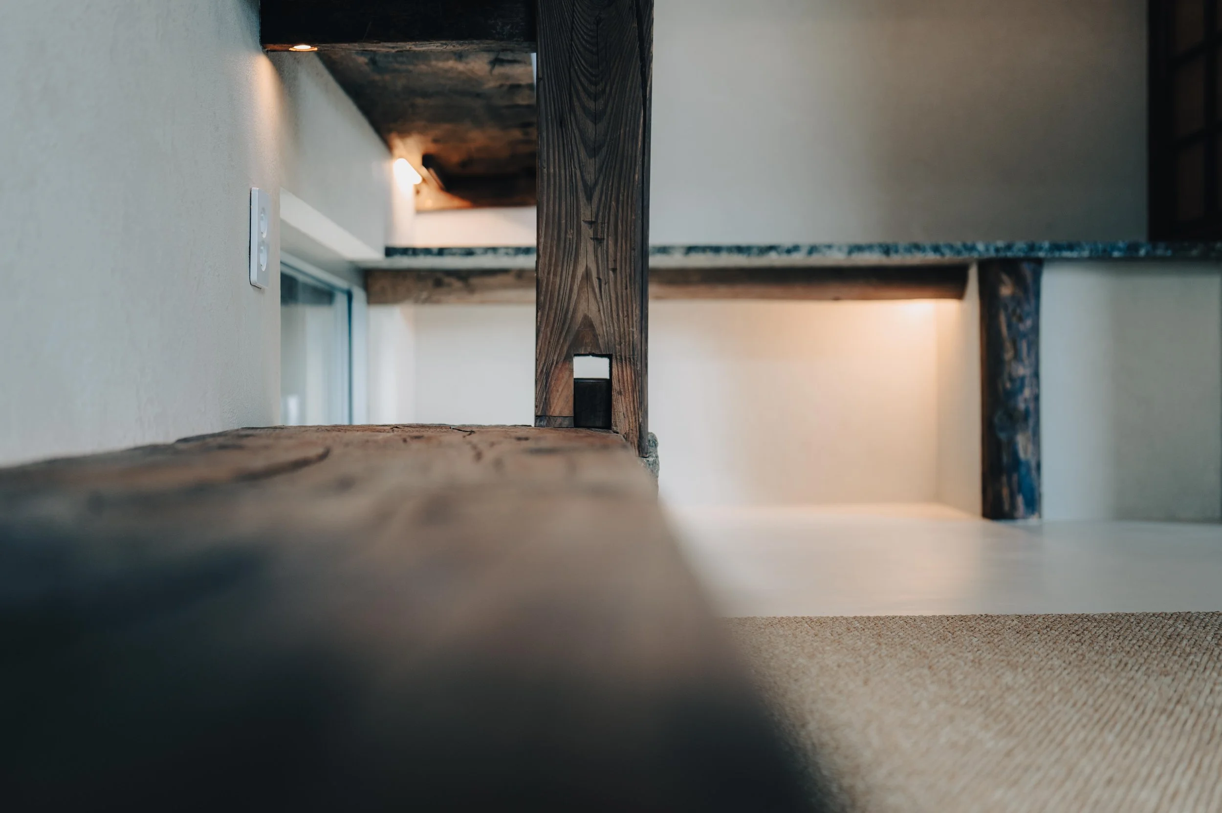 NUUT Aewol 눗애월 Close-up view of a corner of a room showing wooden beams, a wall with an electrical outlet, and soft lighting.