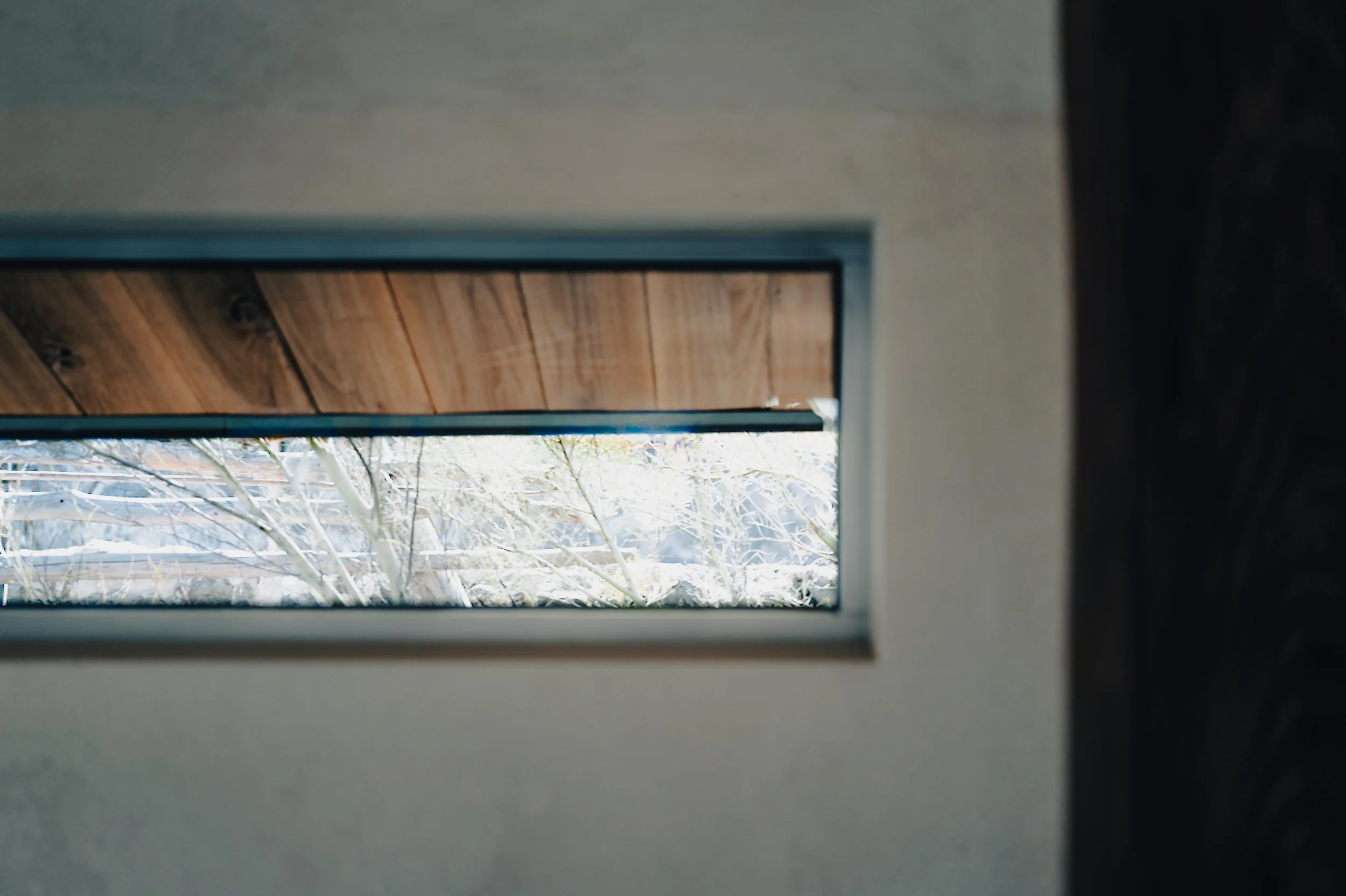 NUUT Aewol 눗애월 View through a rectangular window showing a snowy outdoor scene with leafless trees and a wooden overhang.