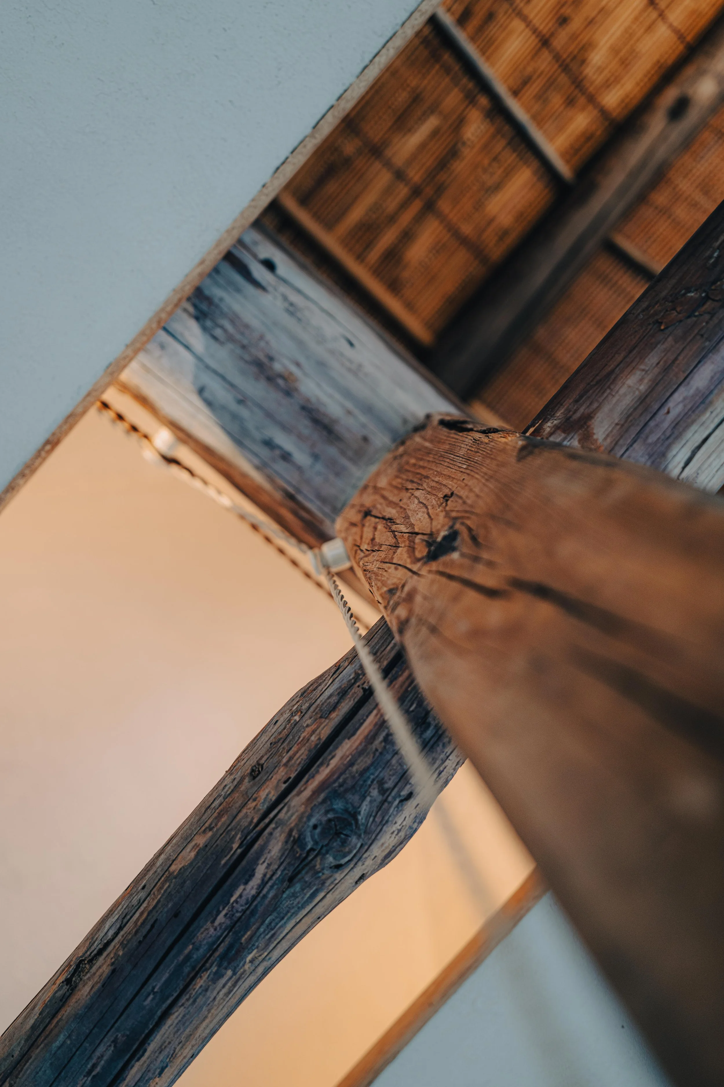 NUUT Aewol 눗애월 Close-up of a wooden beam with a rustic, weathered appearance and visible grain, supporting a structure with wooden panels, seen from underneath.