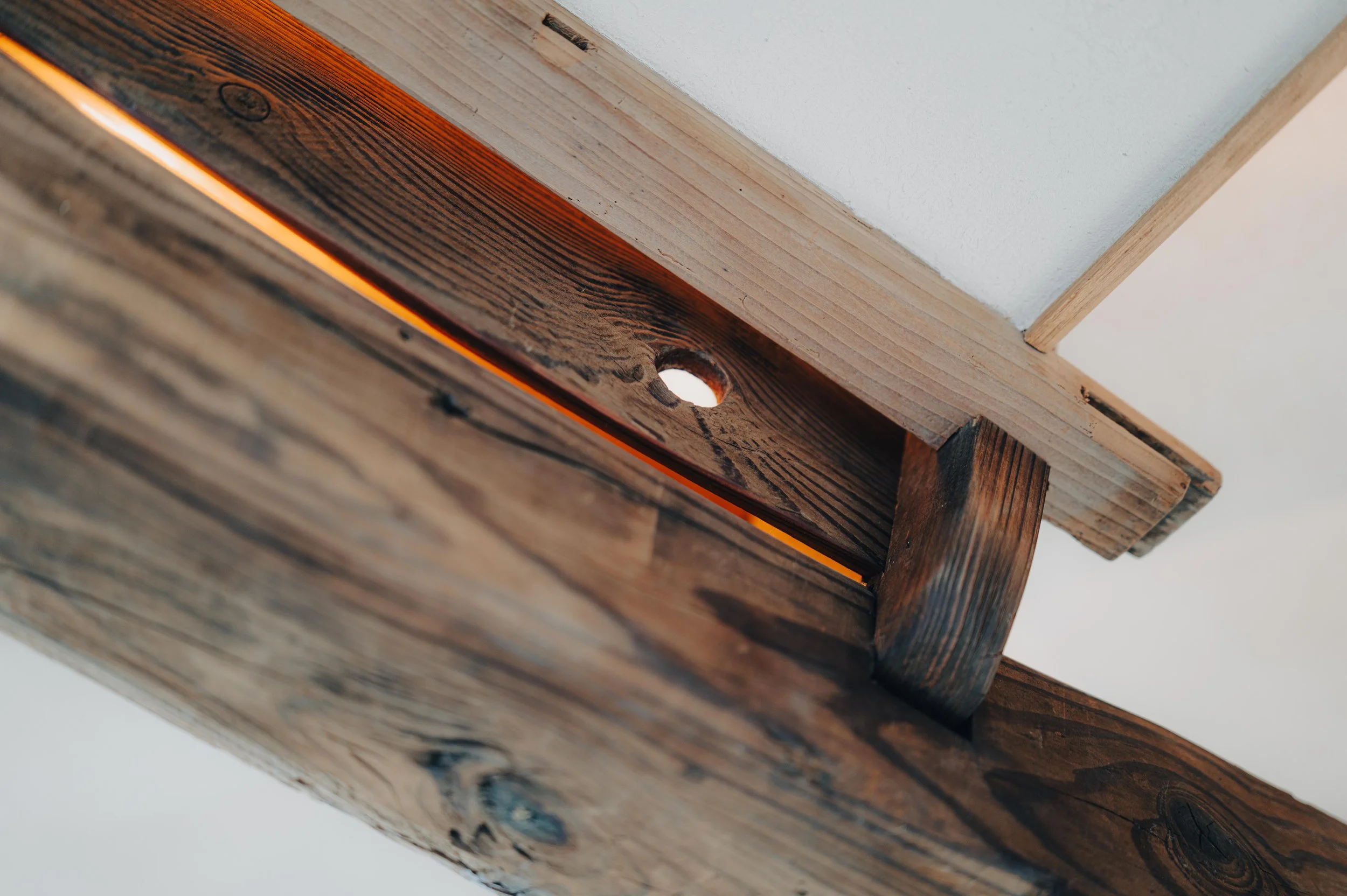 NUUT Aewol 눗애월 Close-up of a wooden ceiling beam with a hole, showing a glow of light through the hole.