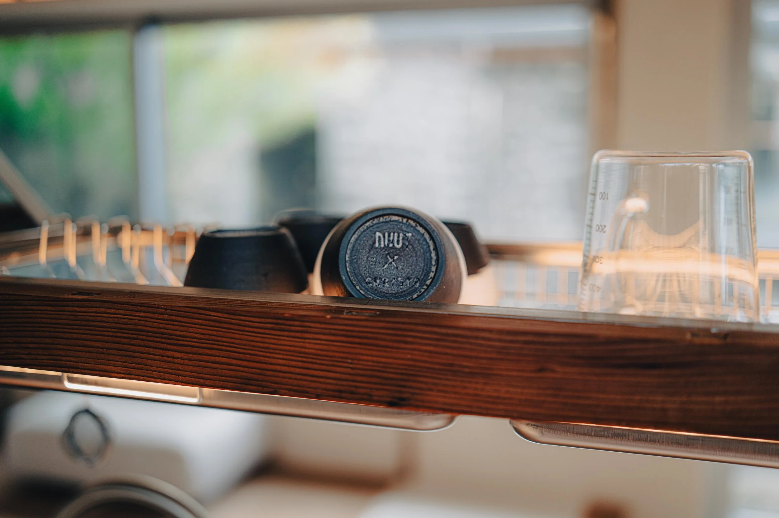 NUUT Aewol 눗애월 Close-up of a wooden dish drying rack with upside-down black bowls and a clear glass on a kitchen countertop.