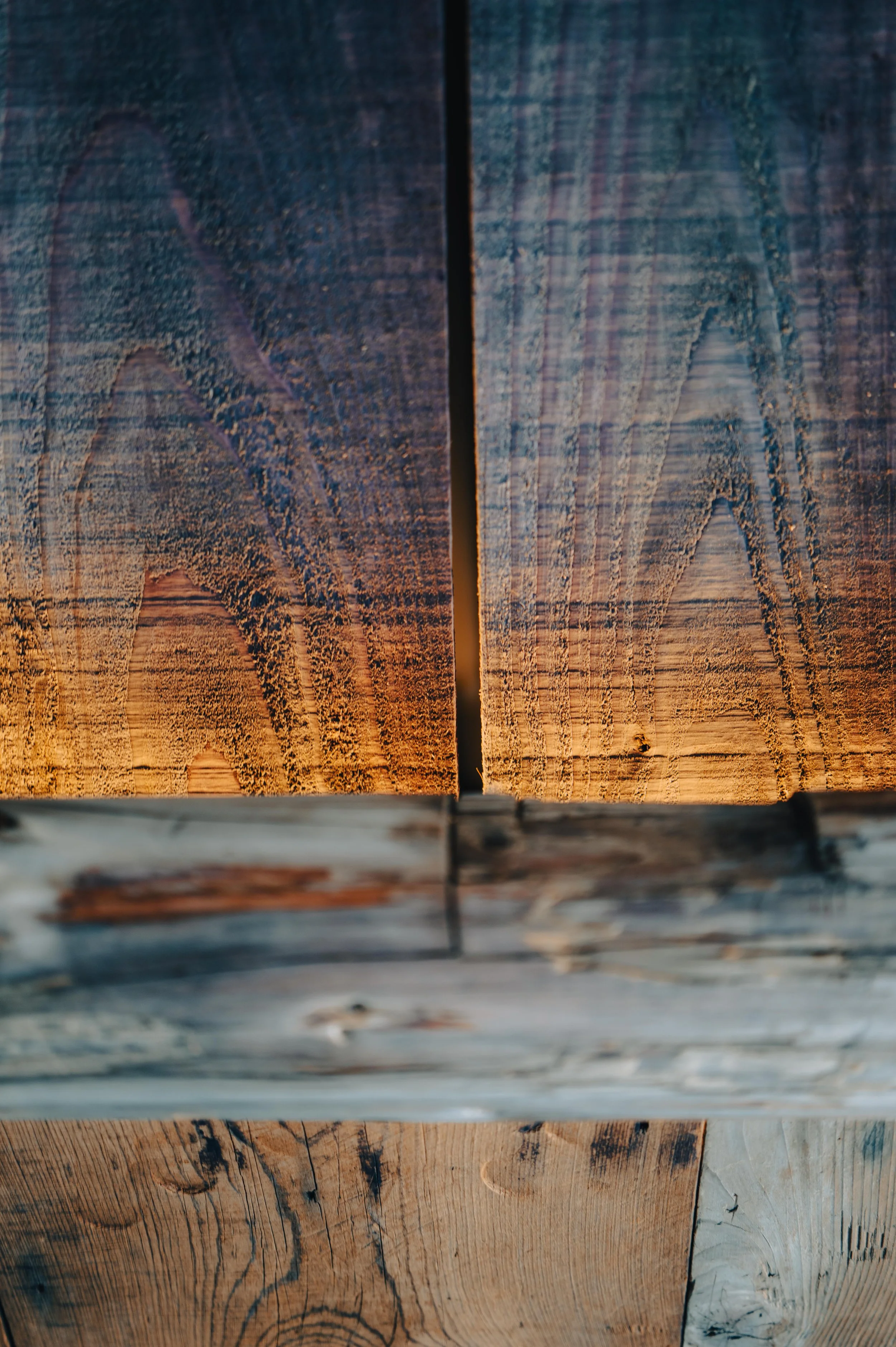Close-up of weathered wooden planks with visible grain patterns and textures, arranged vertically with a narrow gap between the upper two planks.
