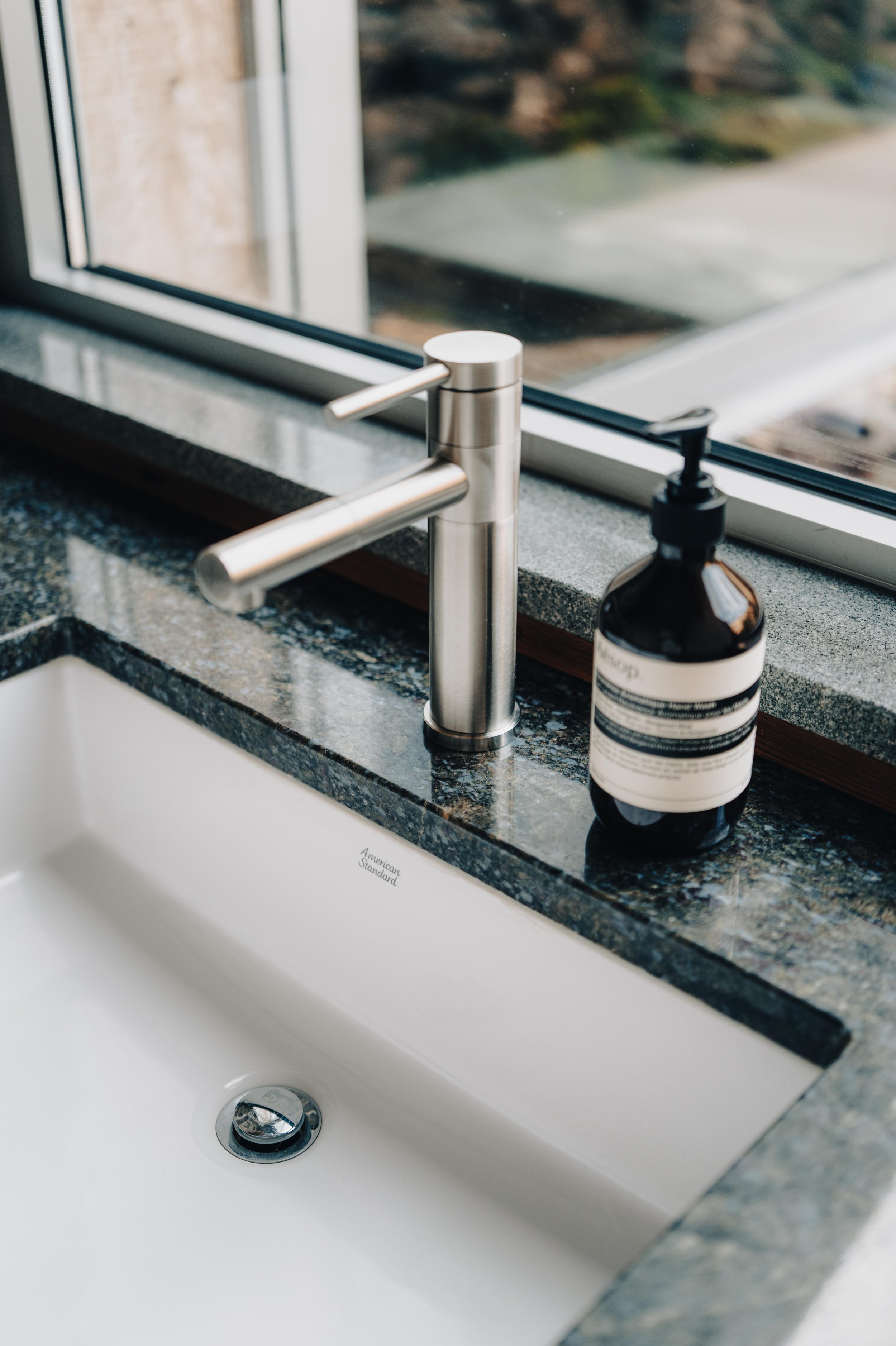 NUUT Aewol 눗애월Close-up of a modern kitchen sink with a stainless steel faucet, a liquid soap dispenser, and a granite countertop near a window.