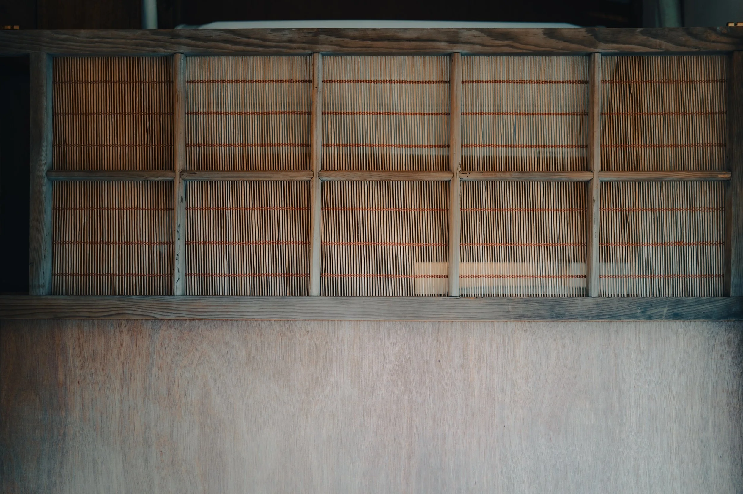 NUUT Aewol 눗애월 Close-up of a traditional shoji screen with a wooden frame and thin bamboo slats, partially revealed through a glass window.