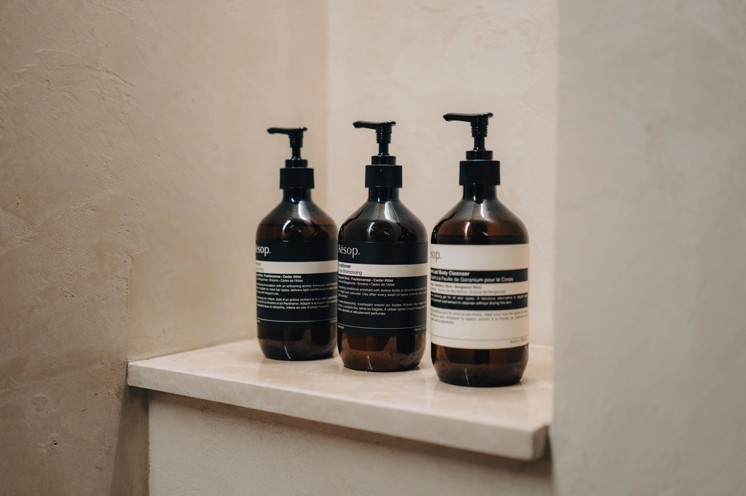 NUUT Aewol 눗애월 Three amber glass bottles with black pump dispensers on a marble shelf, labeled as Aesop body care products.
