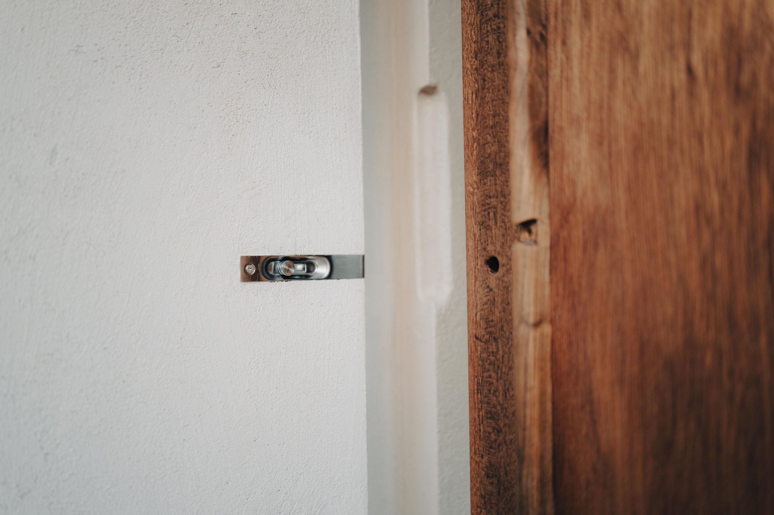 NUUT Aewol 눗애월 Close-up of a metal door latch on a white wall beside a partially visible wooden door frame.
