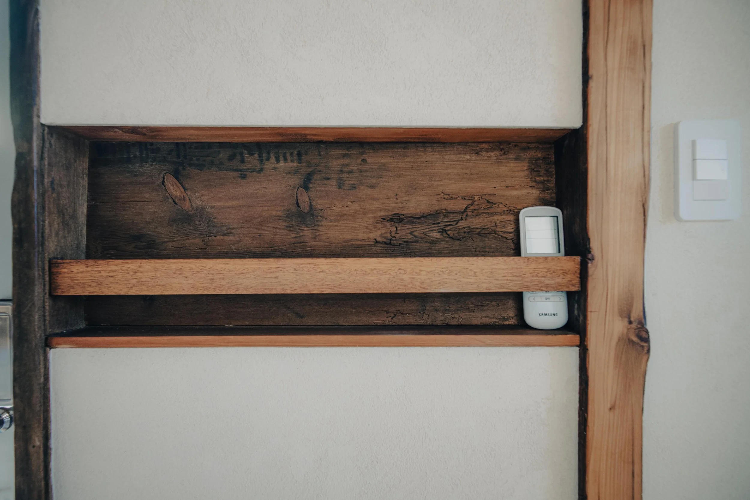 NUUT Aewol 눗애월 Empty wooden shelf with a Samsung remote control placed on the right side.