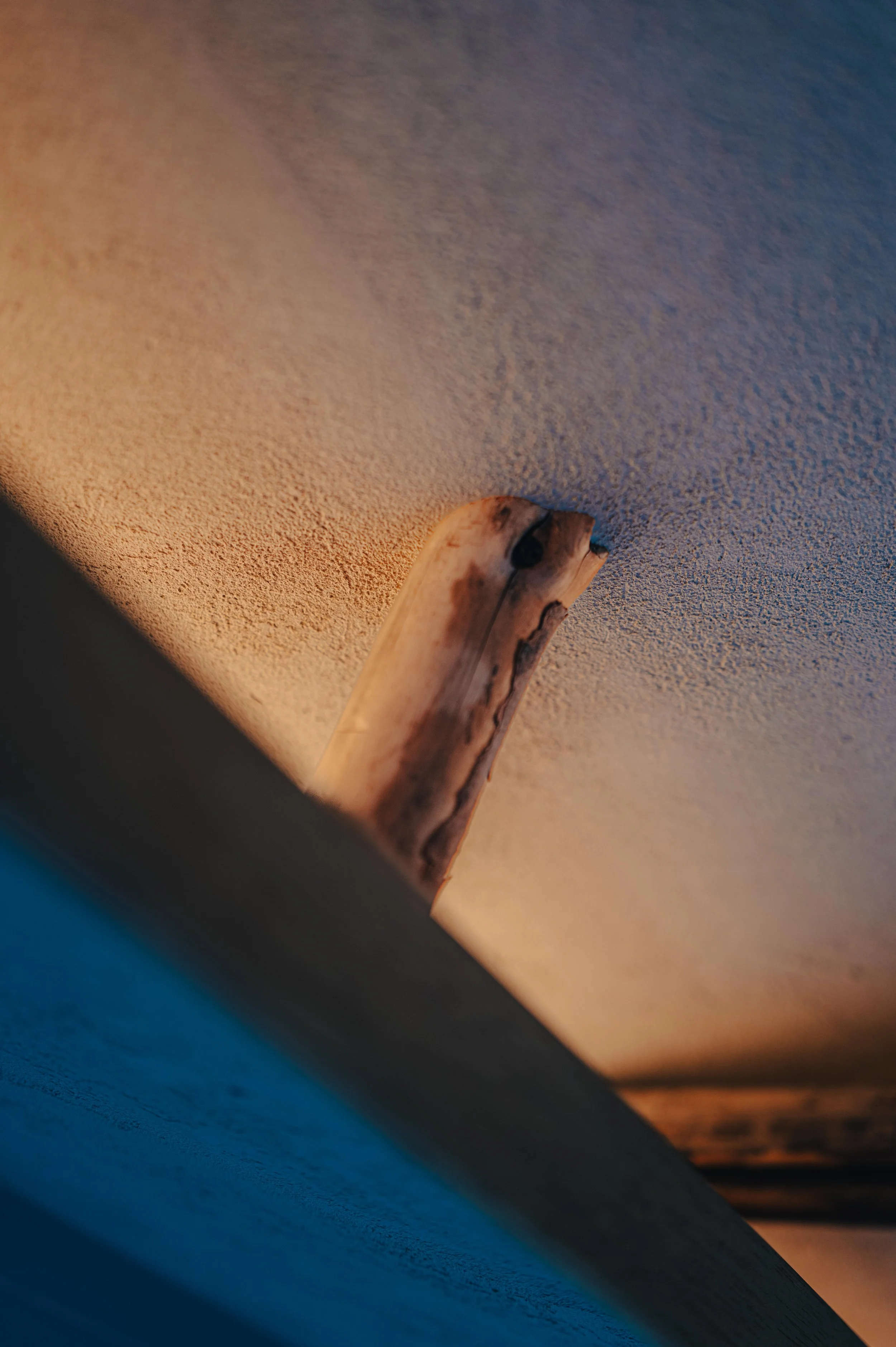 NUUT Aewol 눗애월 Close-up of a wooden object, possibly a handle or piece of driftwood, attached to a textured ceiling with a warm light source.
