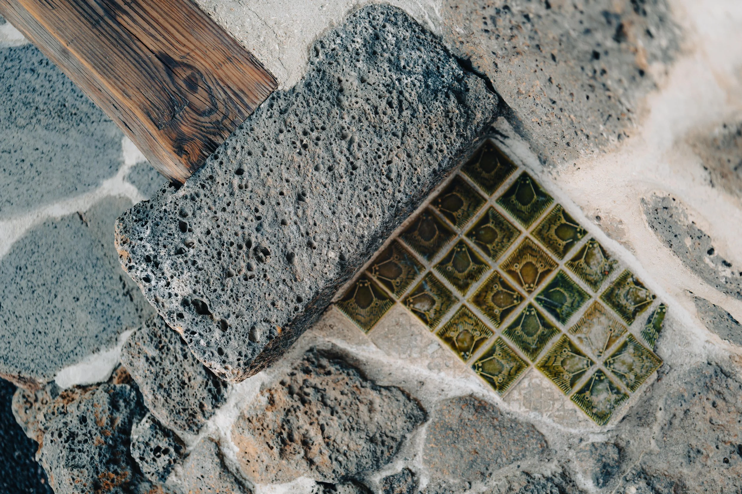 Close-up of a stone wall corner with textured concrete and ceramic tiles featuring a butterfly pattern.