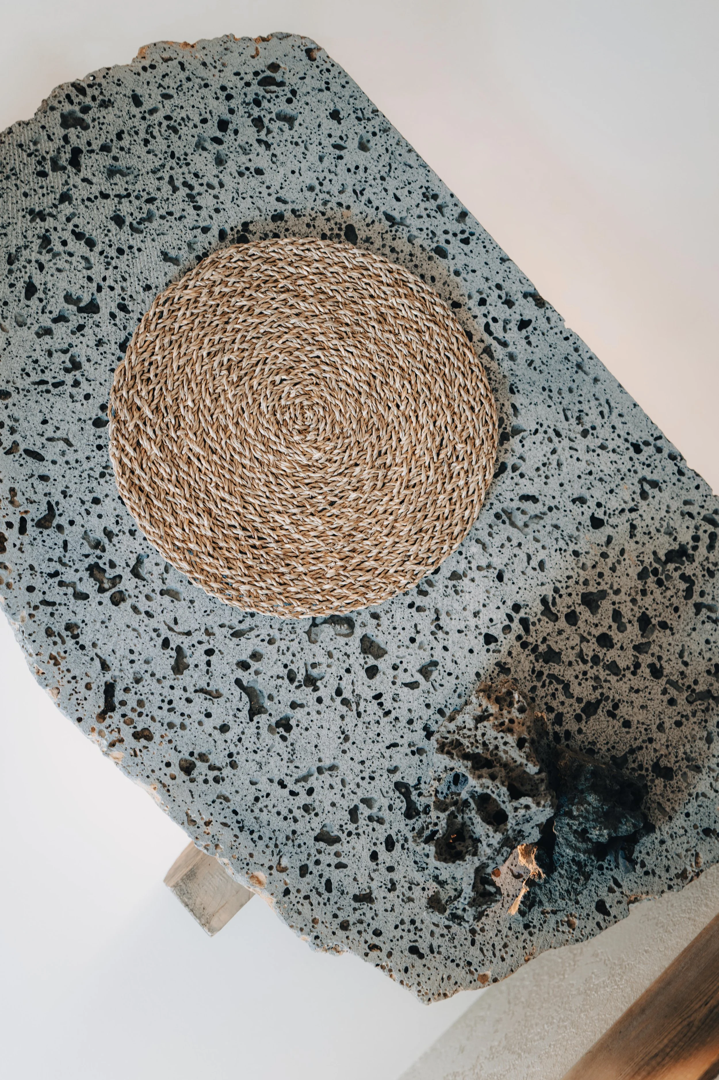NUUT Aewol 눗애월 A round woven straw placemat on a large speckled concrete or terrazzo surface.