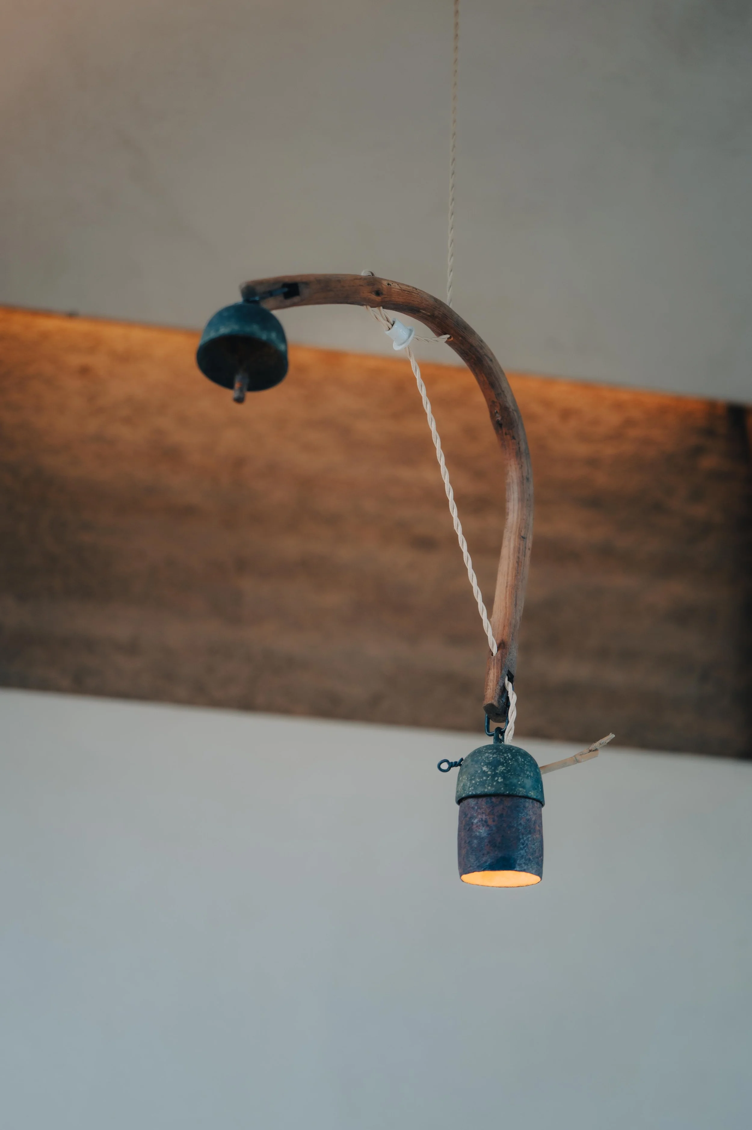 NUUT Aewol 눗애월 Rusty vintage ceiling light fixture with a curved wooden arm, a small metal bell, and a single exposed light bulb, hanging from a white cord.