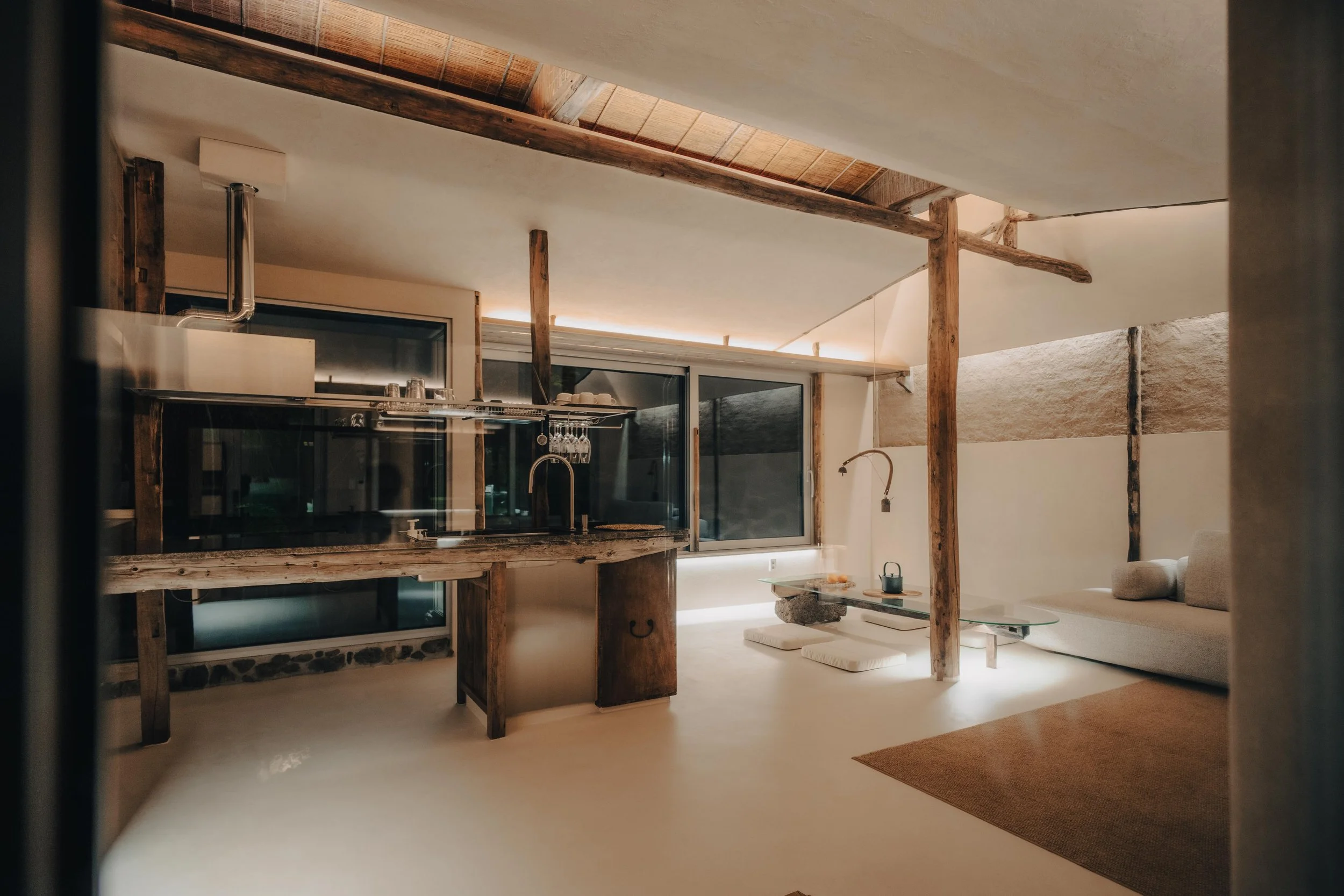 NUUT Aewol 눗애월 Modern living space with rustic wooden beams, minimalist furniture, and large windows.