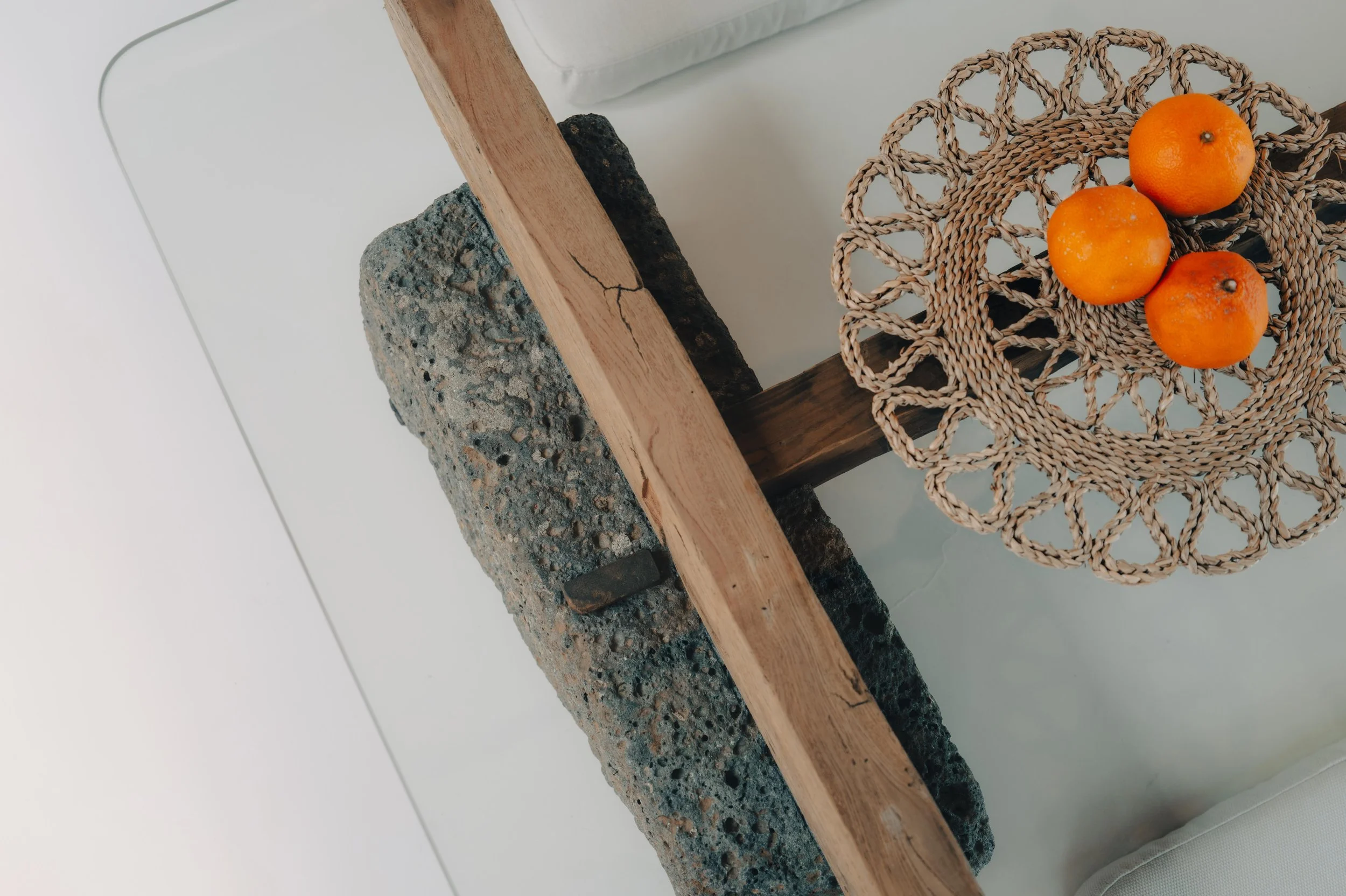 NUUT Aewol 눗애월 Top-down view of a small round woven basket with three oranges inside placed on a wooden side table with a concrete base, against a white background.