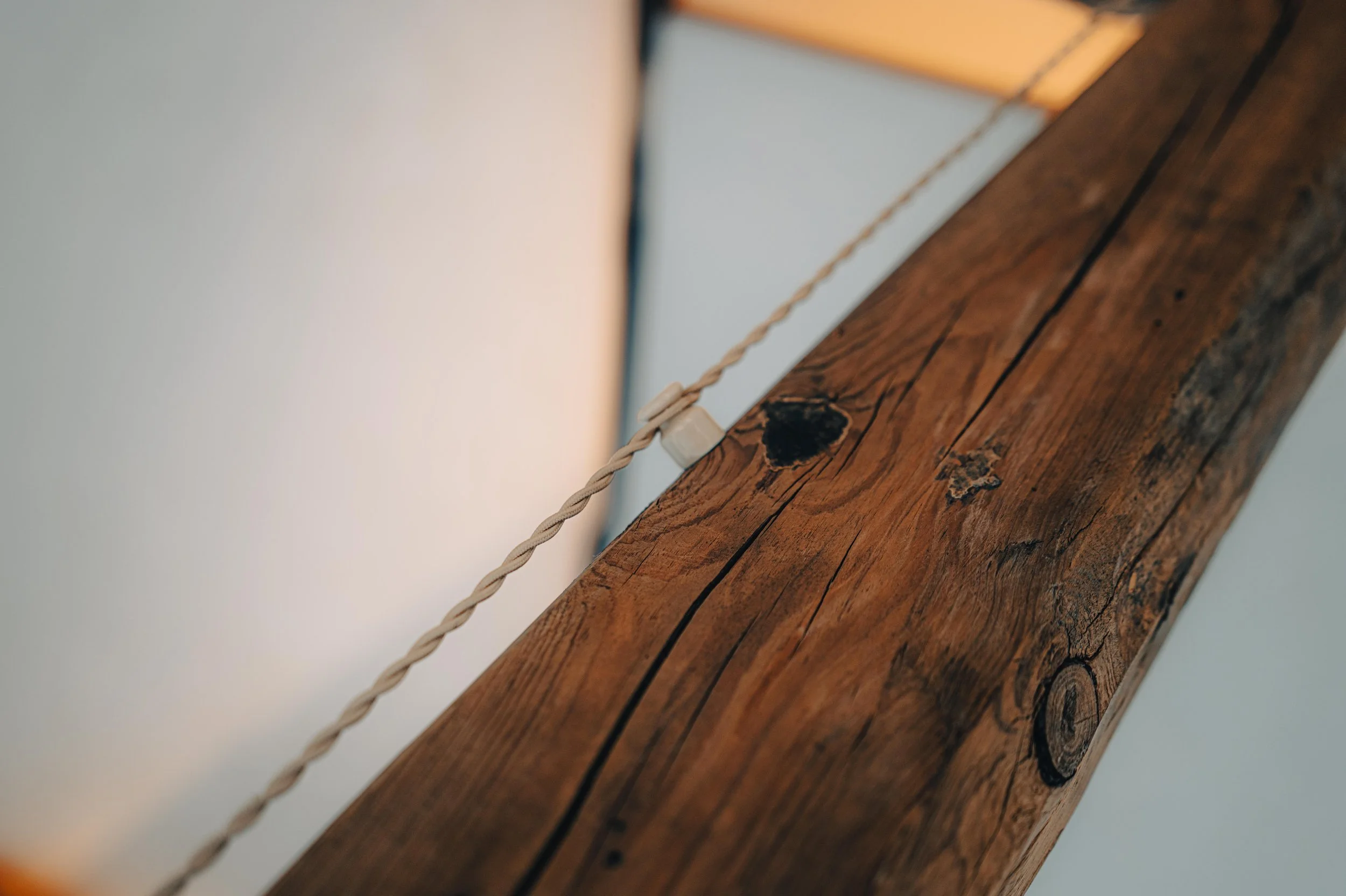 NUUT Aewol 눗애월 Close-up of a wooden beam with a twisted rope passing through a small wooden pulley attached to it.