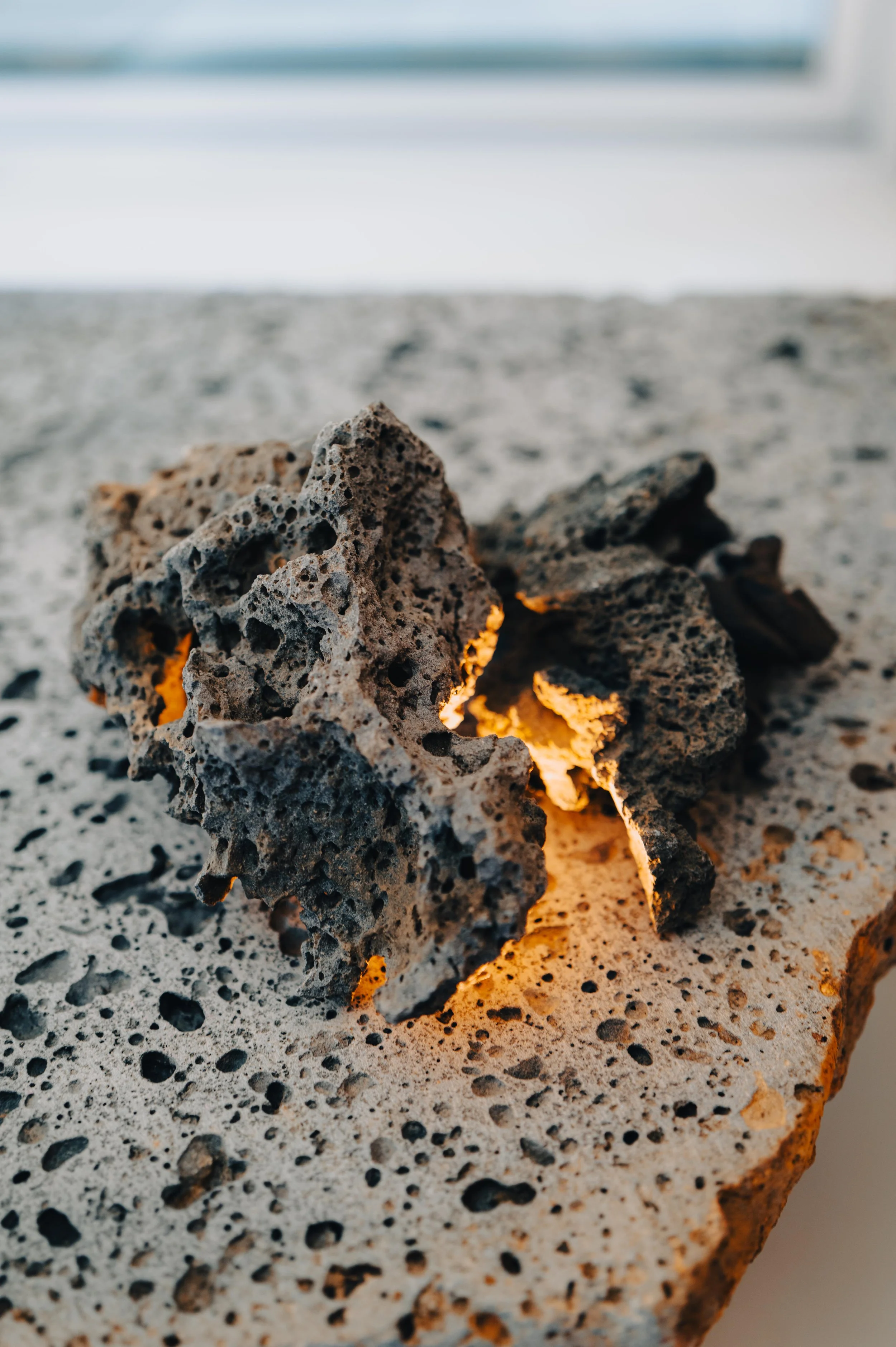 NUUT Aewol 눗애월 Close-up of two volcanic rocks with glowing lava inside, on a textured surface, with a blurred background.