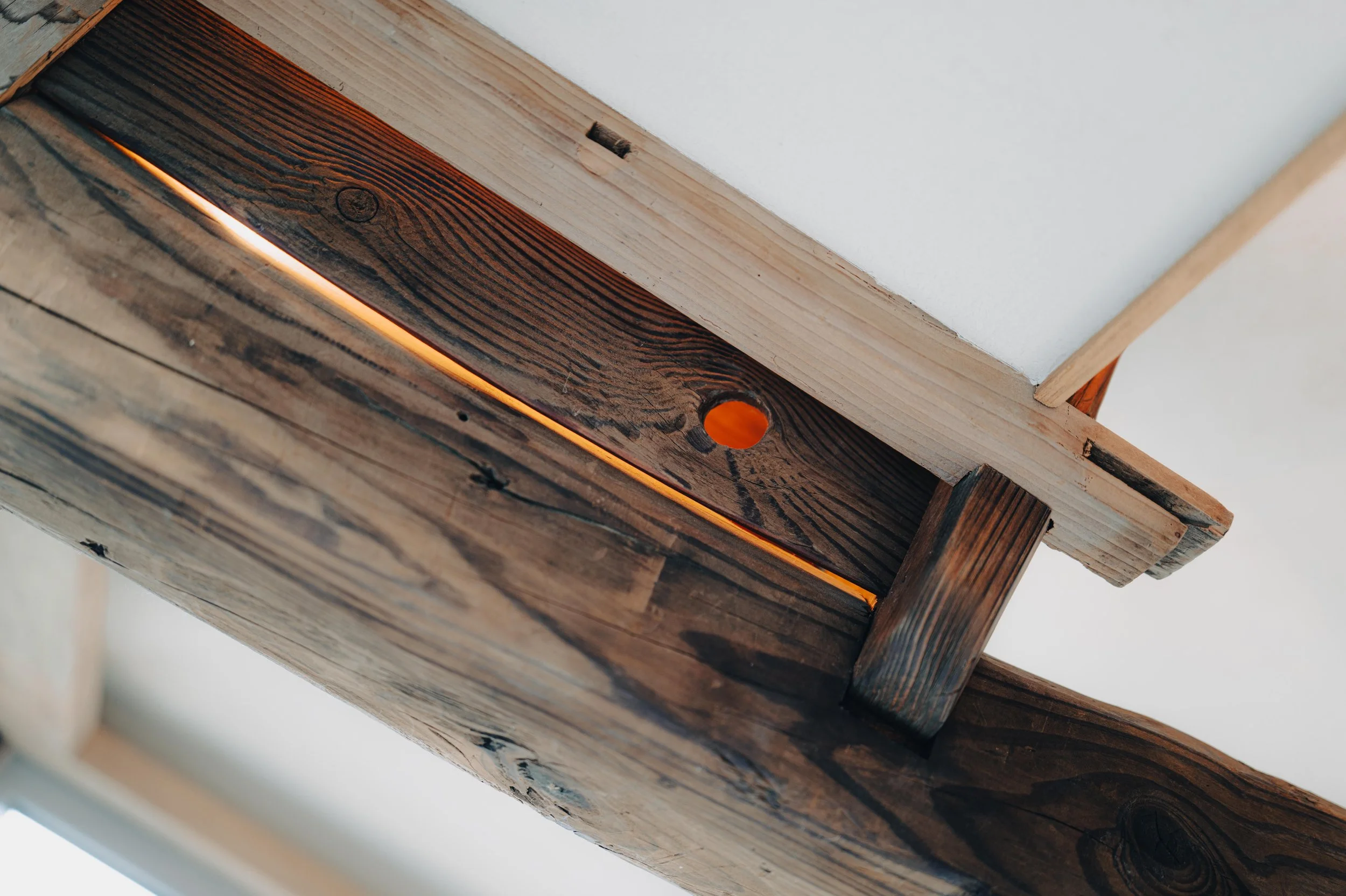 NUUT Aewol 눗애월 Close-up view of a wooden ceiling beam with a gap revealing an orange light source behind.